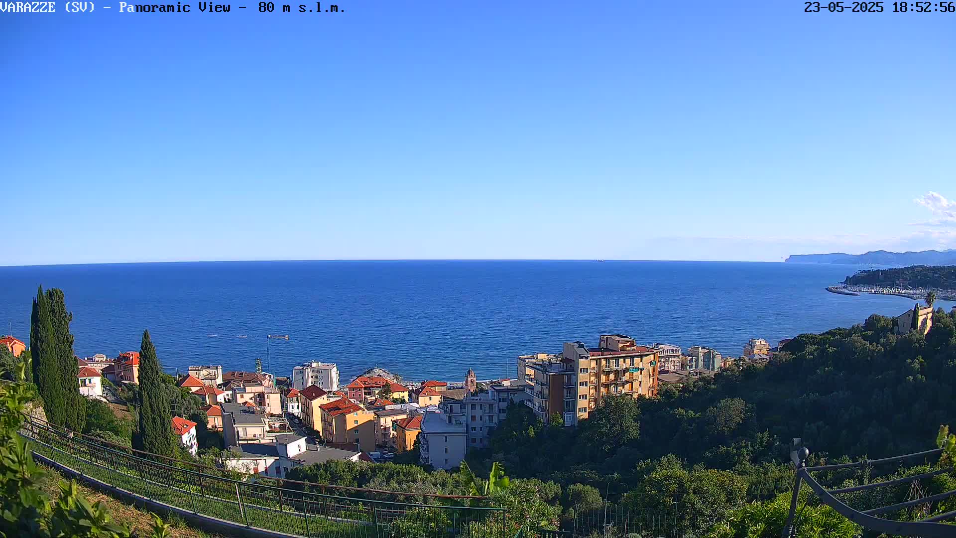 A coastal town with colorful buildings is nestled on a hillside overlooking a calm, blue sea under a clear, sunny sky.