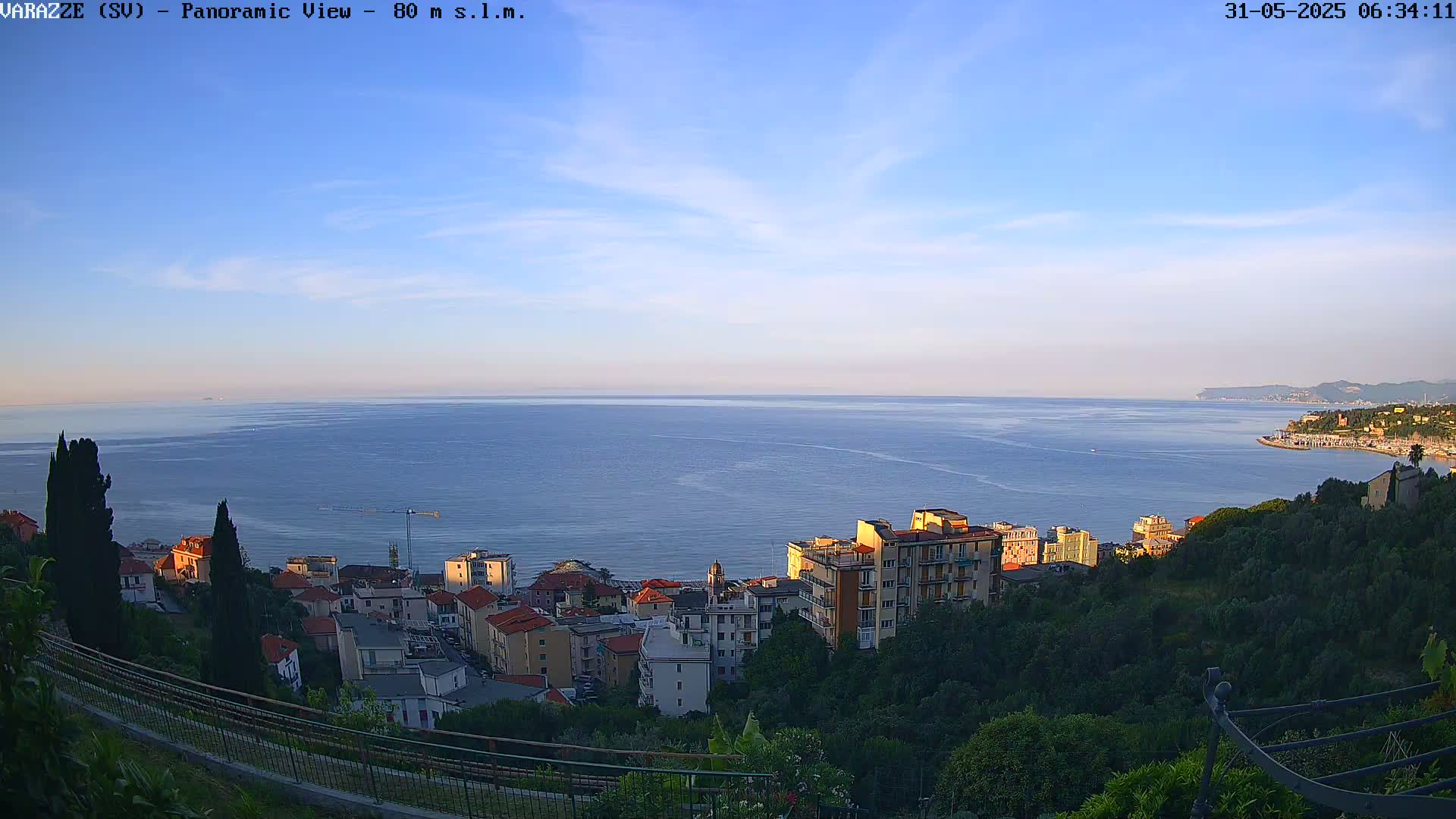 A coastal town nestled on a hillside overlooks a calm sea under a clear, bright sky.