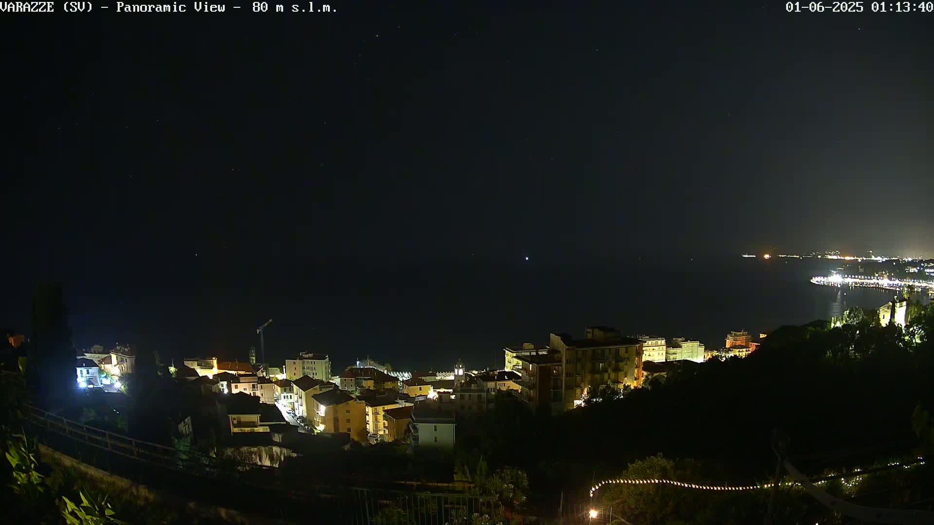 A nighttime panoramic view of a coastal town with its lights illuminated against a dark, clear sky over calm water.