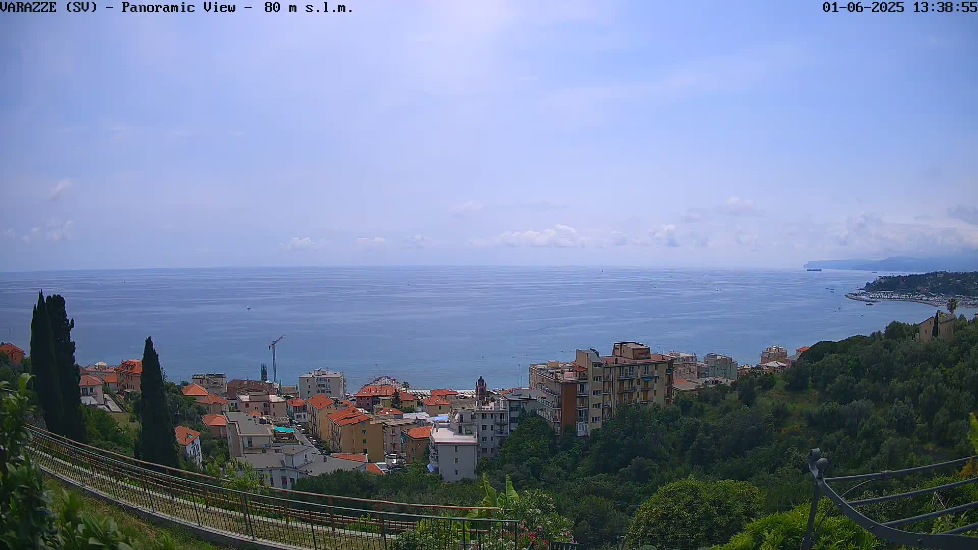 A panoramic view of a coastal town on a partly cloudy day, showcasing a calm blue sea extending to the horizon.