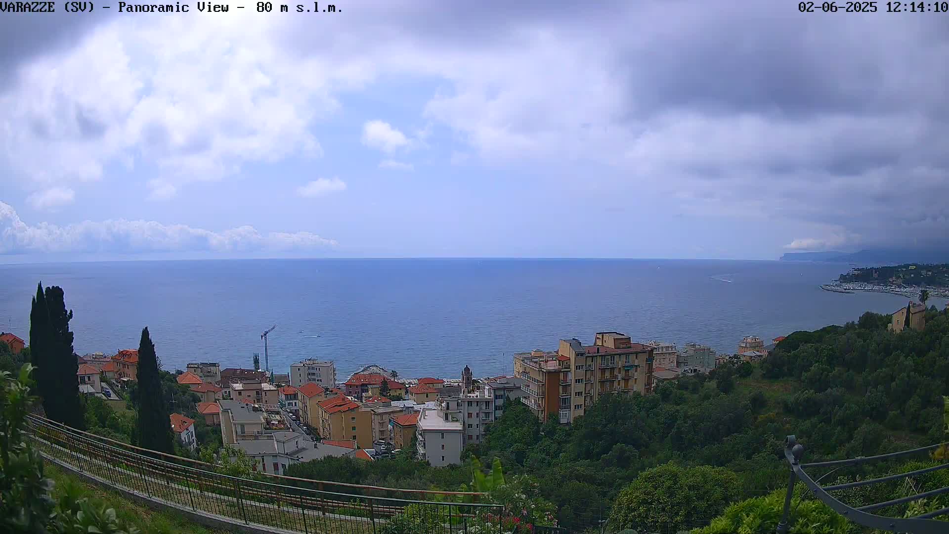A coastal town nestled on a hillside overlooks a calm sea under a partly cloudy sky.