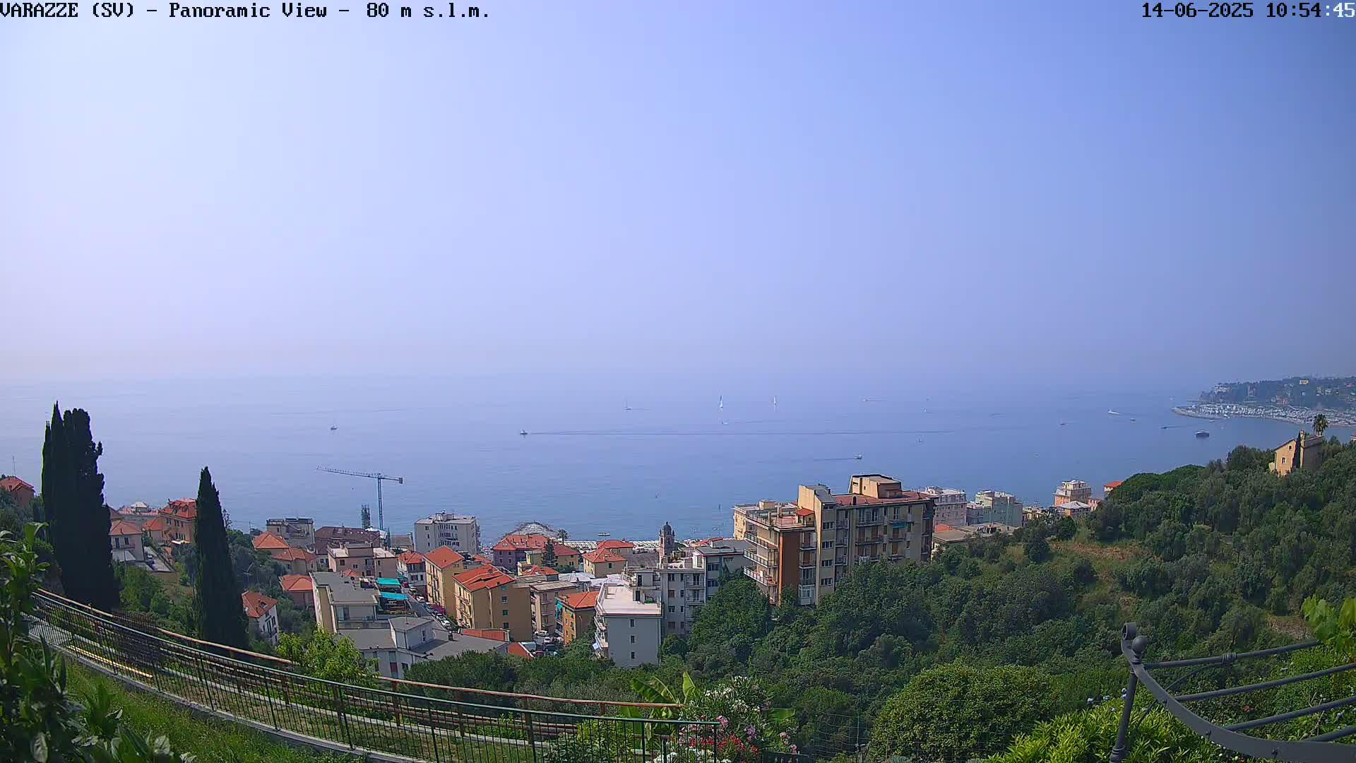 A panoramic view of a coastal town nestled on a hillside overlooking a calm blue sea under a clear sky.