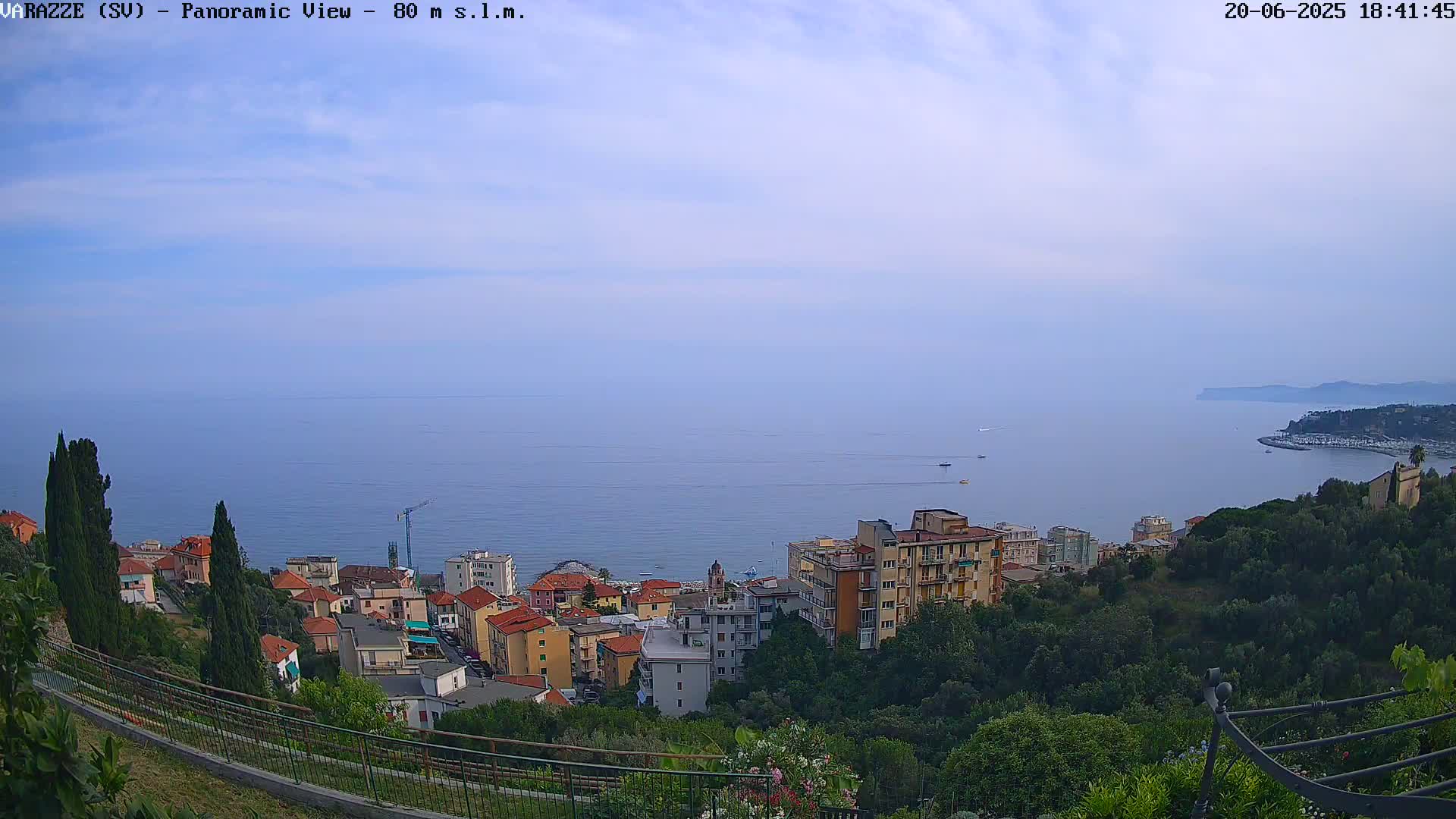 A panoramic view of a coastal town nestled on a hillside overlooking a calm sea under a hazy sky.