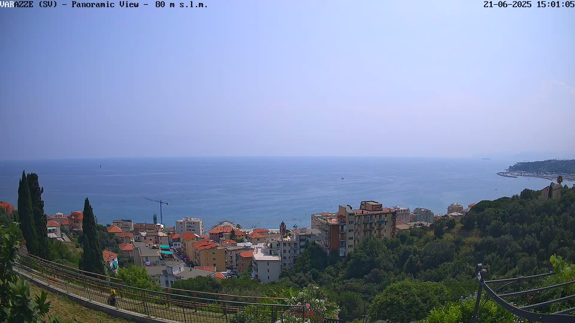 A coastal town nestled on a hillside overlooks a calm, blue sea under a clear sky.