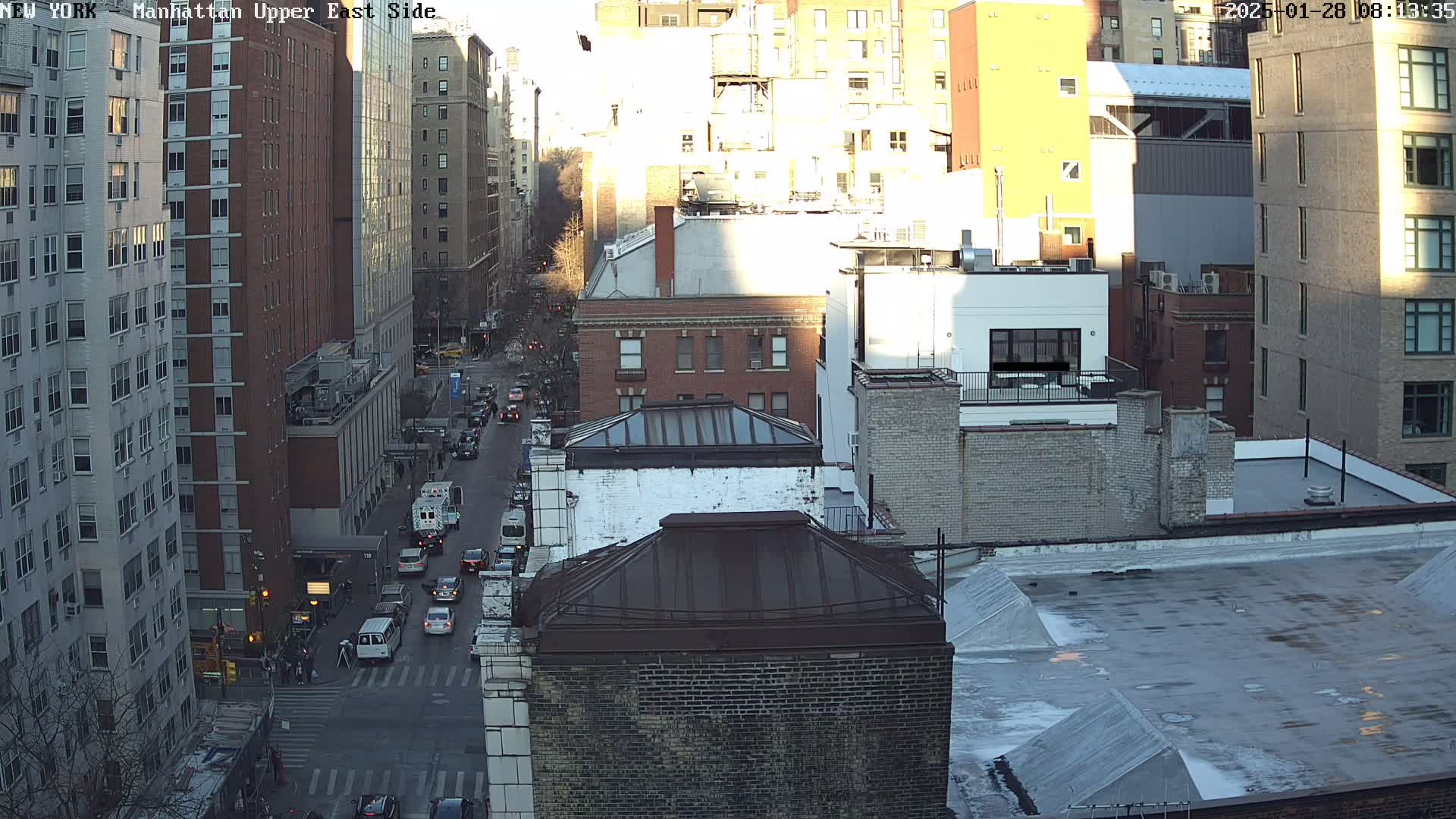 An aerial view of a city street with several tall buildings on a partly sunny day.