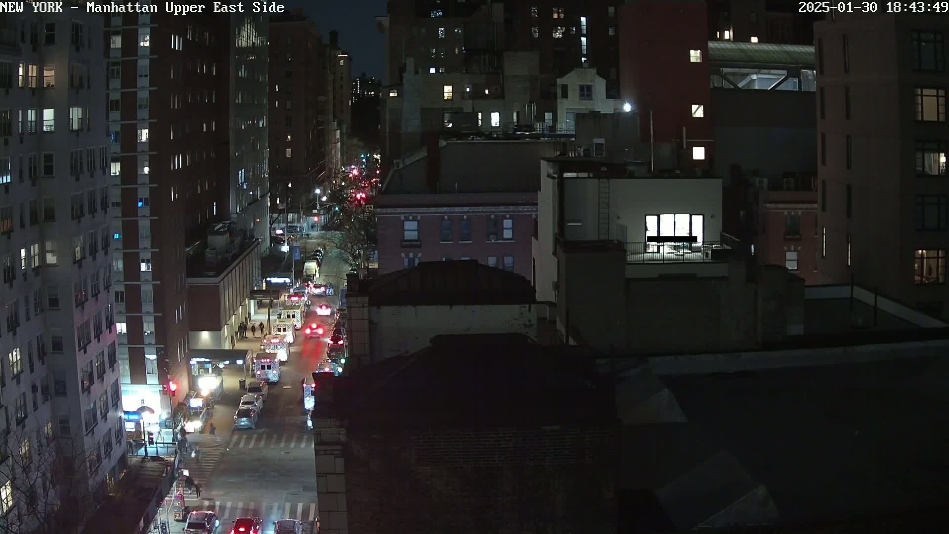 A nighttime aerial view of a city street, showing several buildings and traffic moving along a road under dark, clear skies.