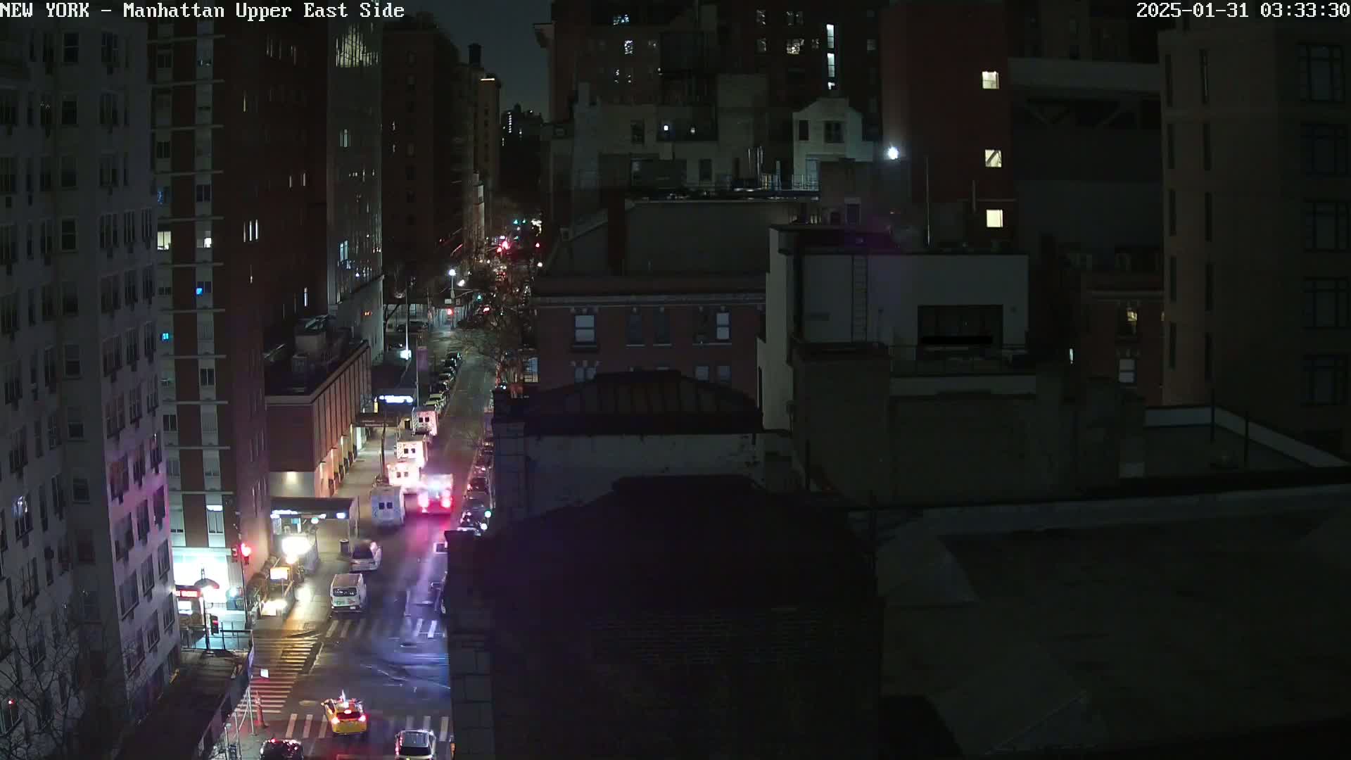 A nighttime aerial view shows a city street with several vehicles, including emergency vehicles, under dark, clear skies.