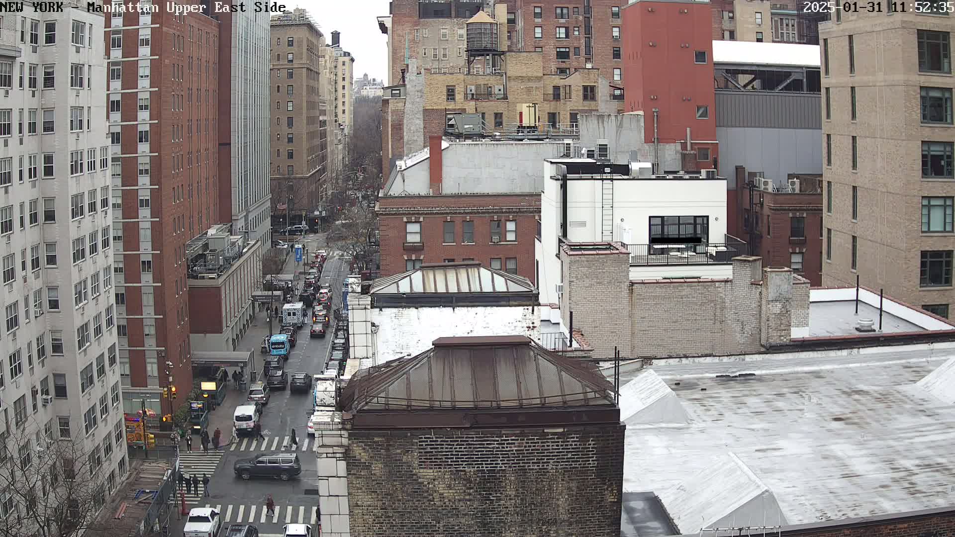 A high-angle view of a city street, showing several brick buildings and cars on an overcast day.