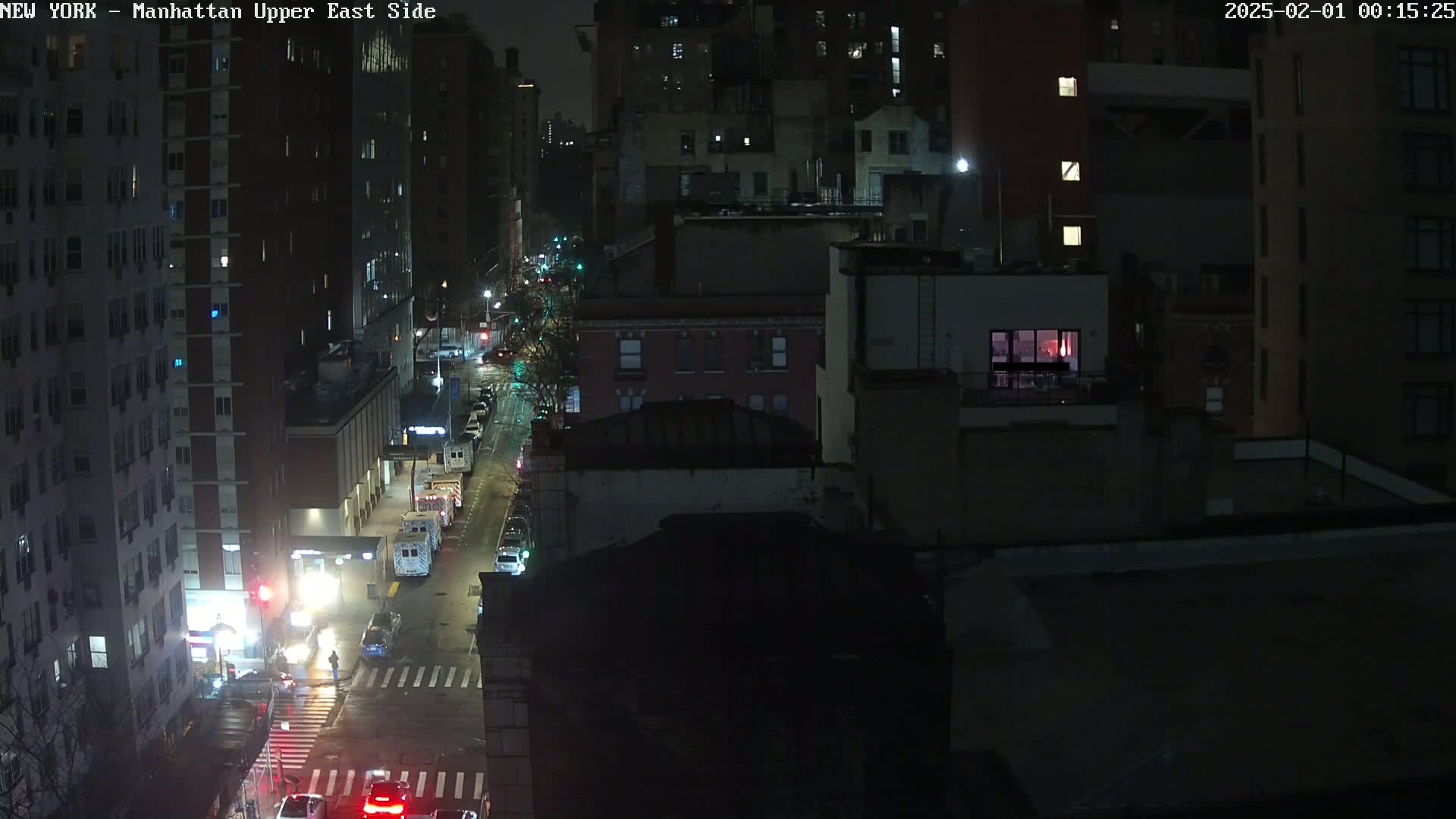 A nighttime, aerial view of a city street with several cars and buildings, illuminated by streetlights.
