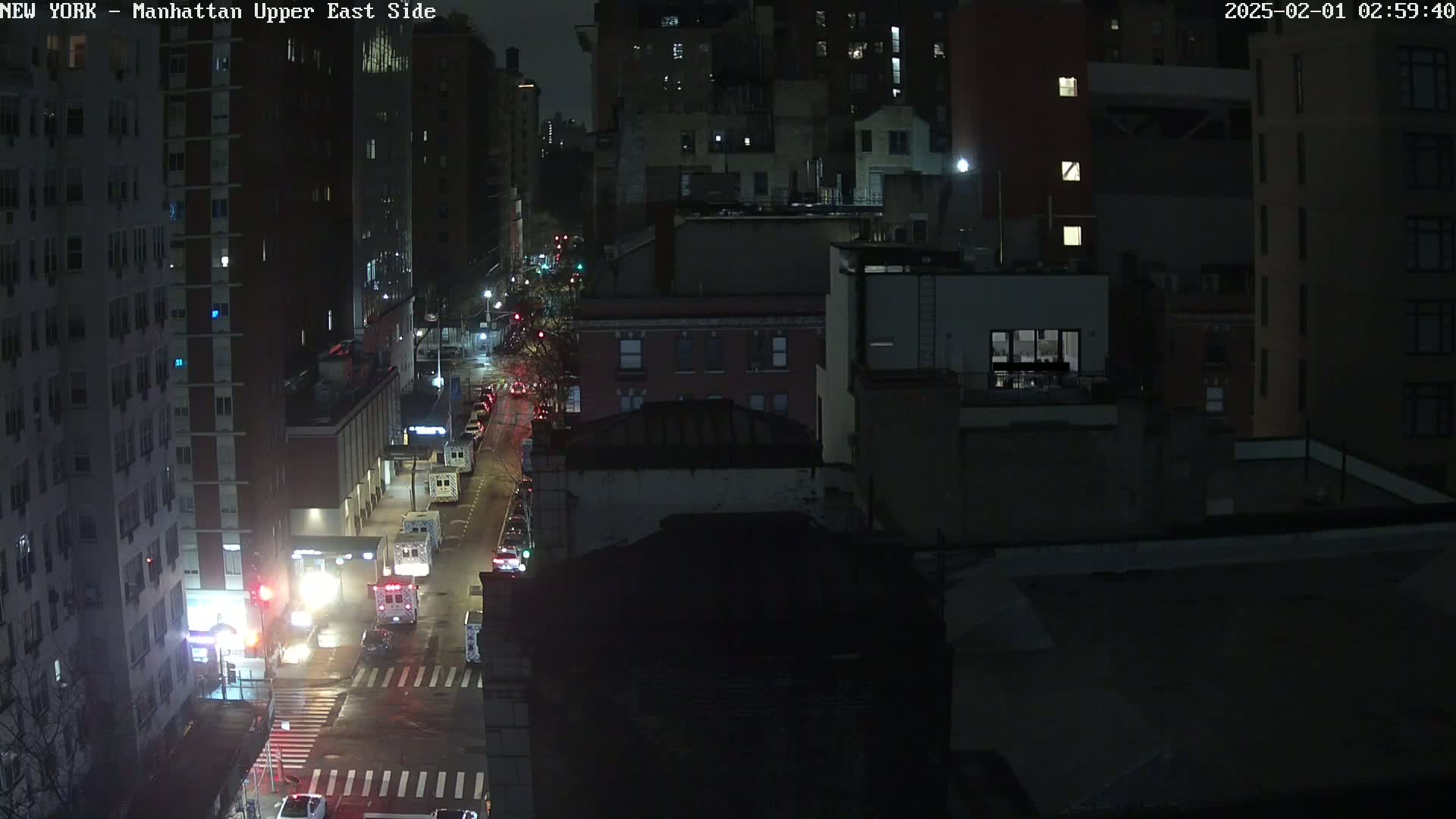 A nighttime, rain-slicked city street scene shows several buildings, vehicles, and traffic lights.