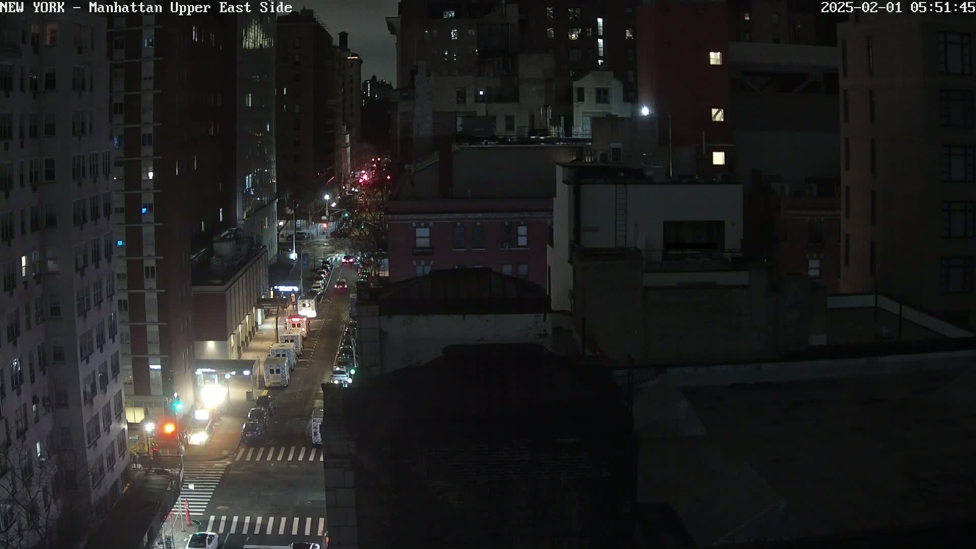 A nighttime, high-angle view of a city street with several vehicles and tall buildings under a dark sky.
