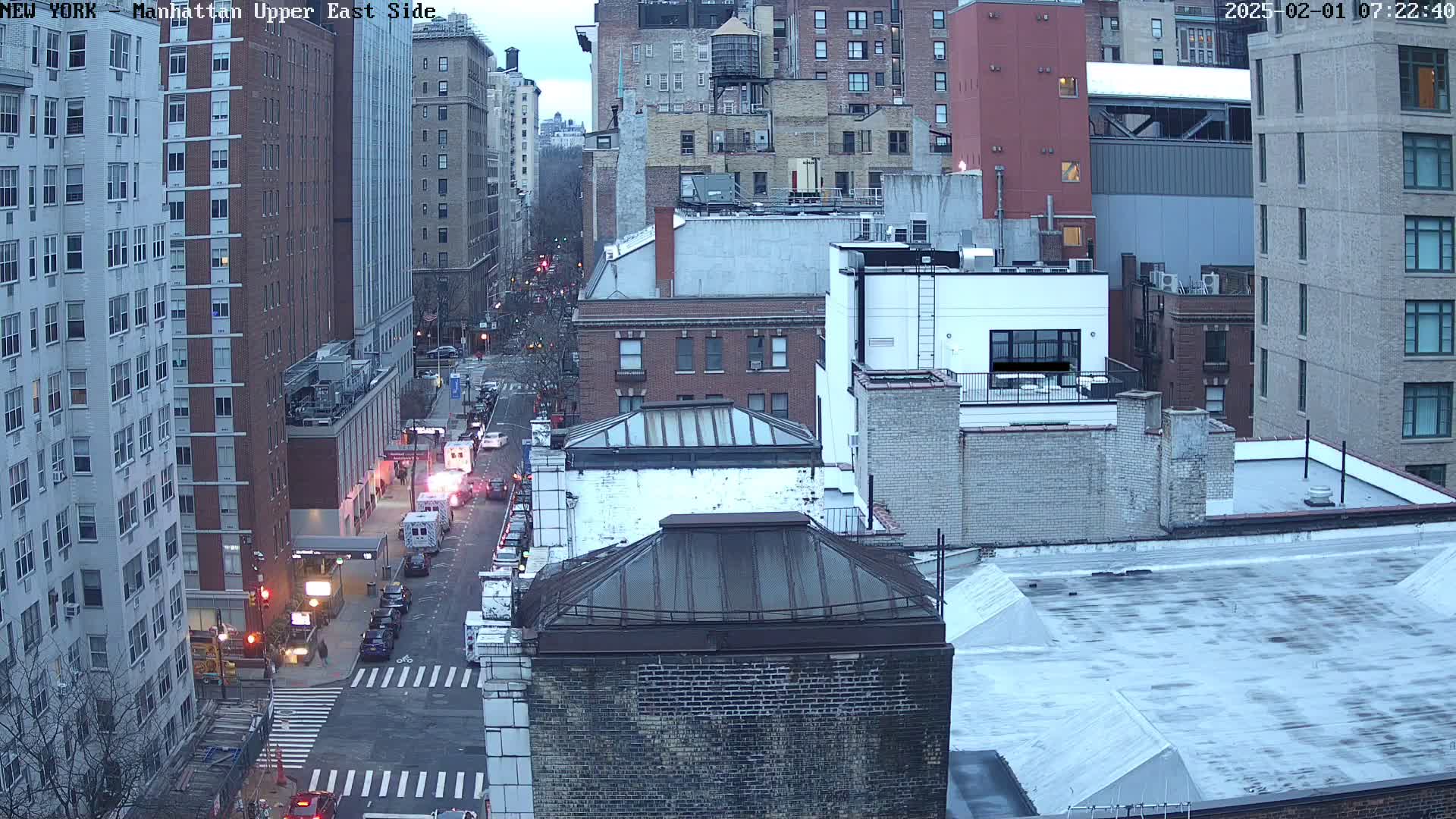 An aerial view of city buildings on an overcast day, showing a street with several cars and emergency vehicles.
