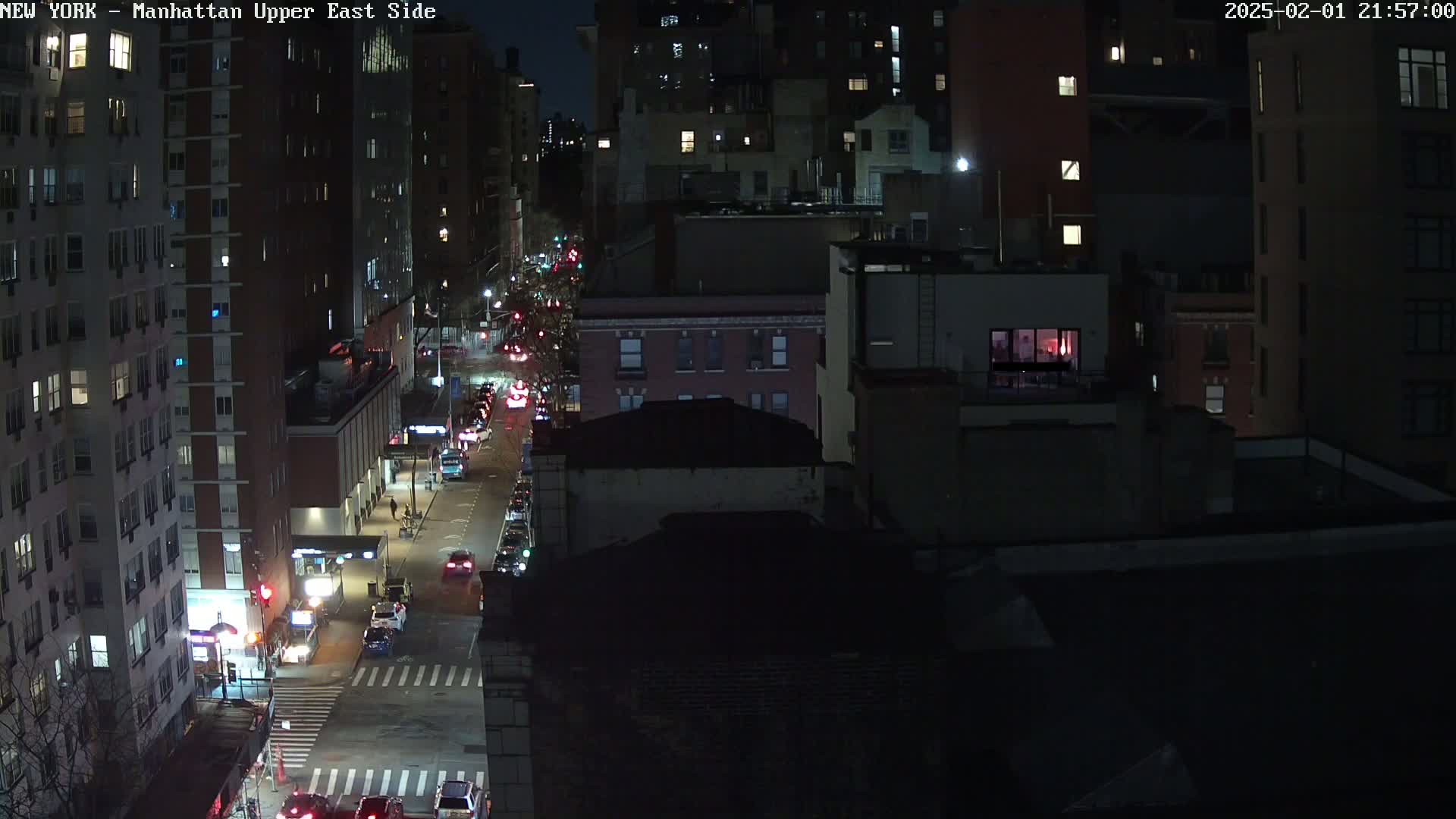 A nighttime, high-angle view of a city street with cars driving on it, lined with tall buildings.