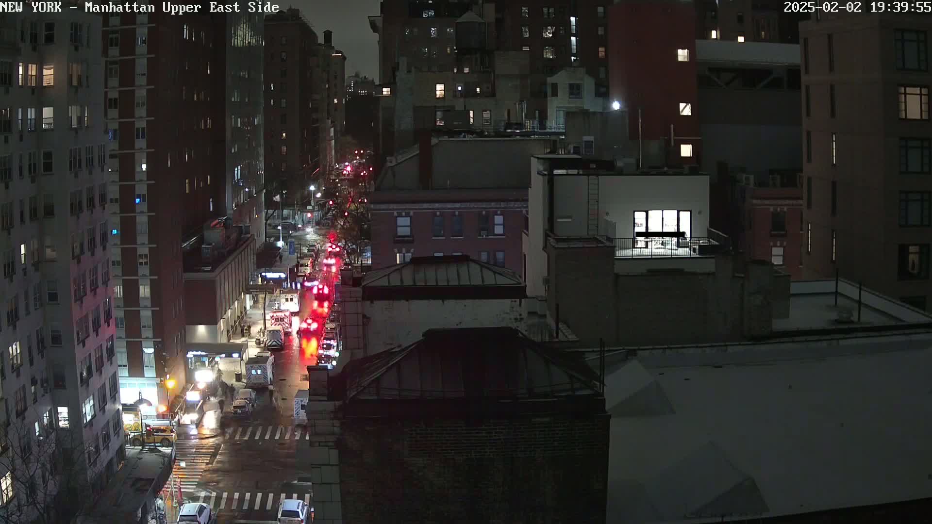 A nighttime aerial view of a city street with several emergency vehicles, possibly responding to an incident, under snowy conditions.