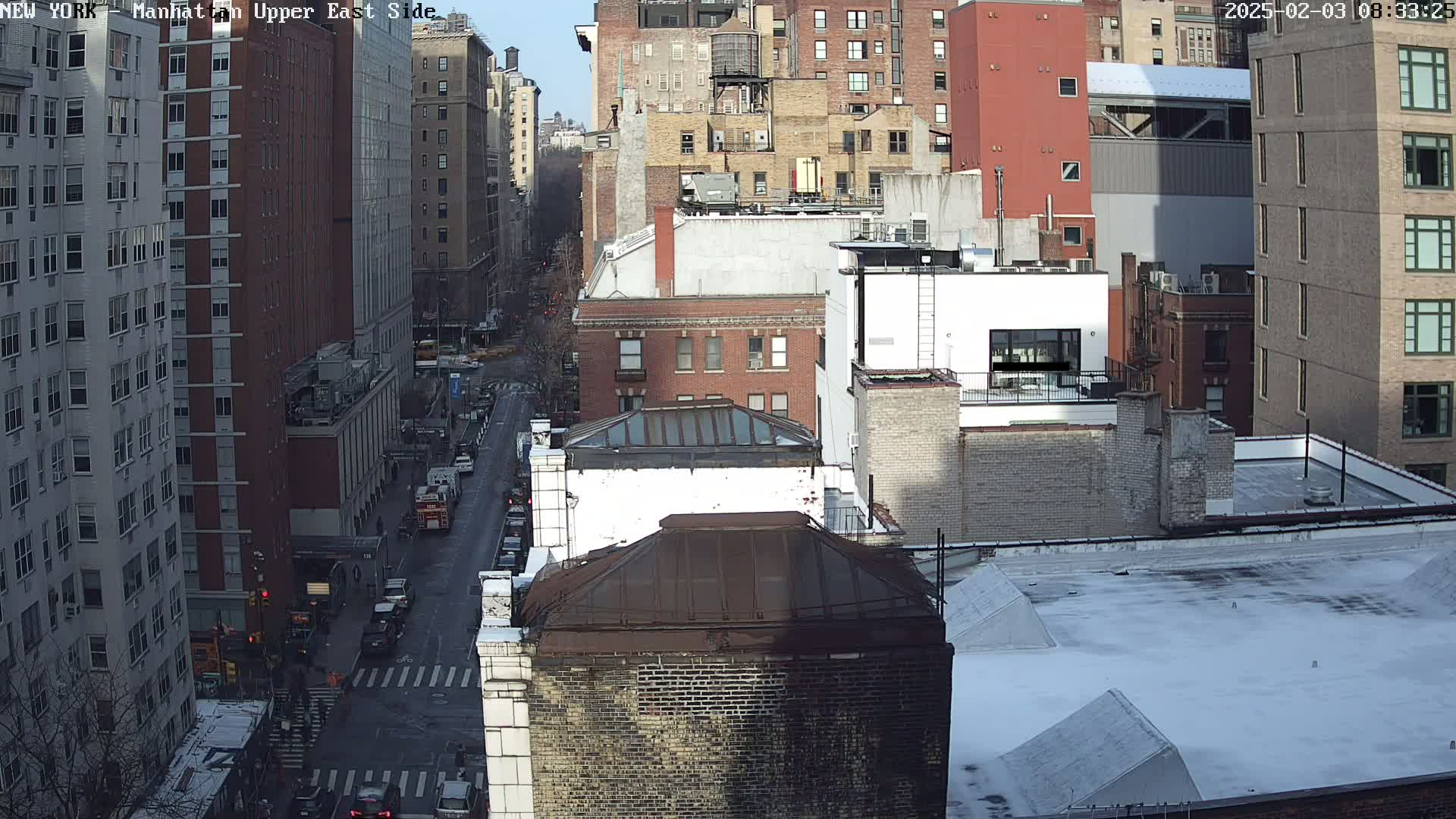 A sunny winter day view of a city street, showing several multi-story buildings and vehicles traveling on the street below.