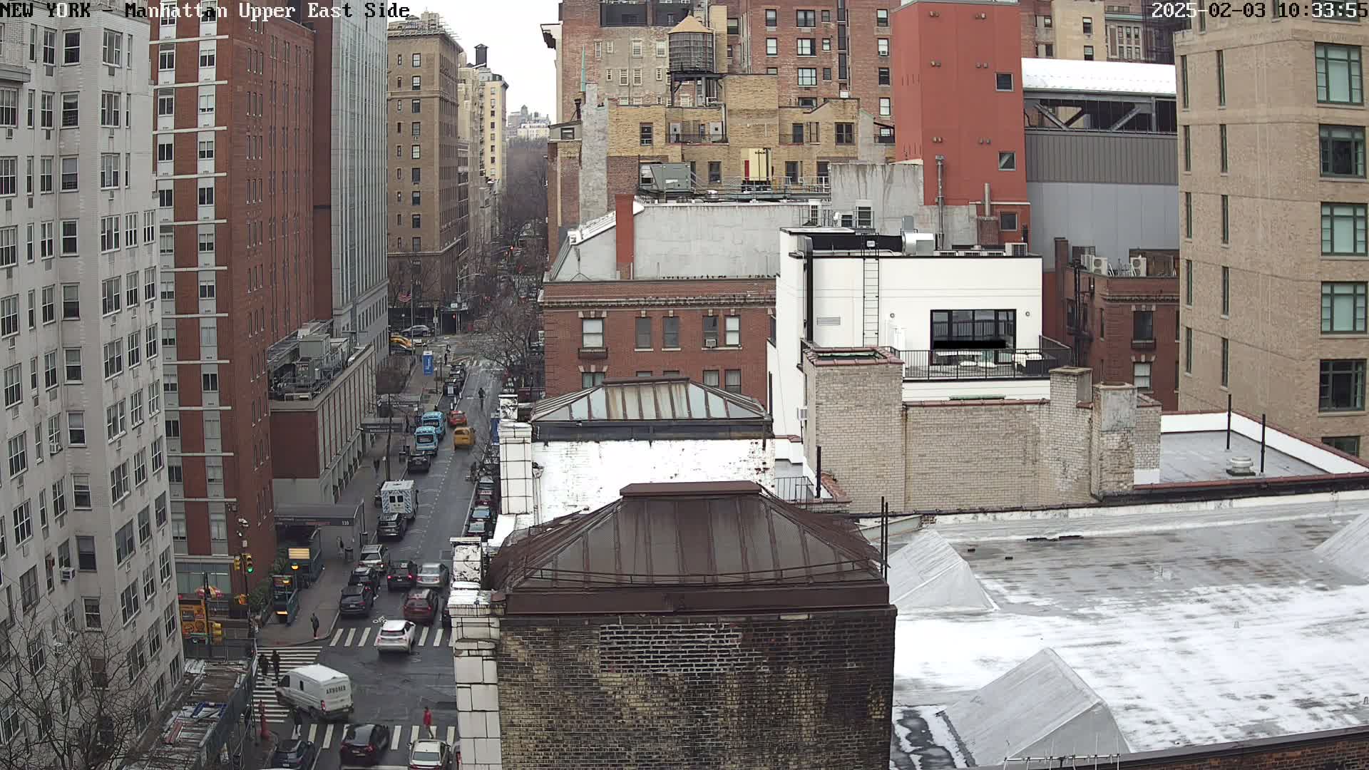 A high-angle view of a city street scene on an overcast day, showing several multi-story buildings and vehicles traveling on a street below.