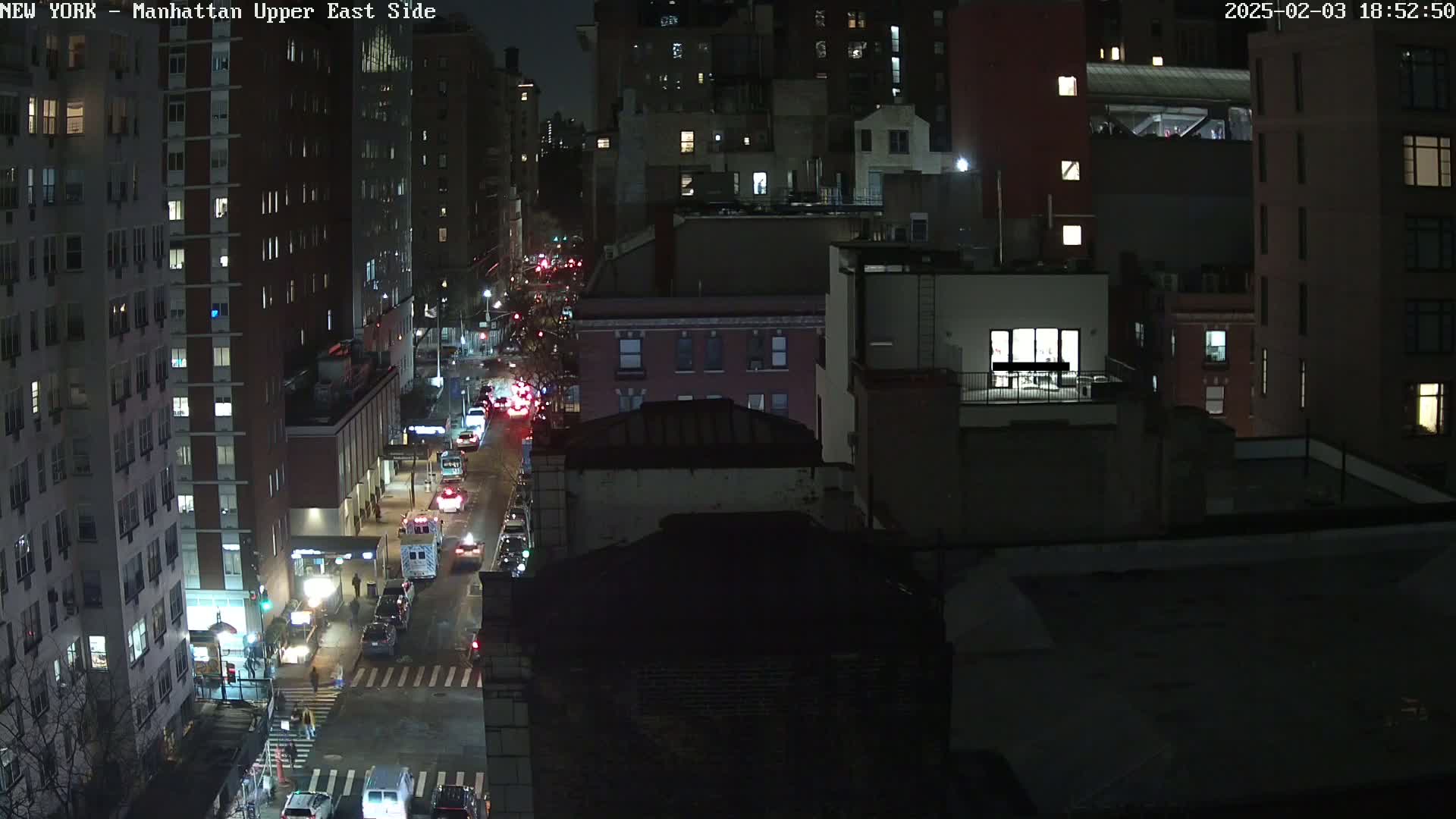 A nighttime aerial view of a city street with traffic, showing several multi-story buildings under a dark sky.
