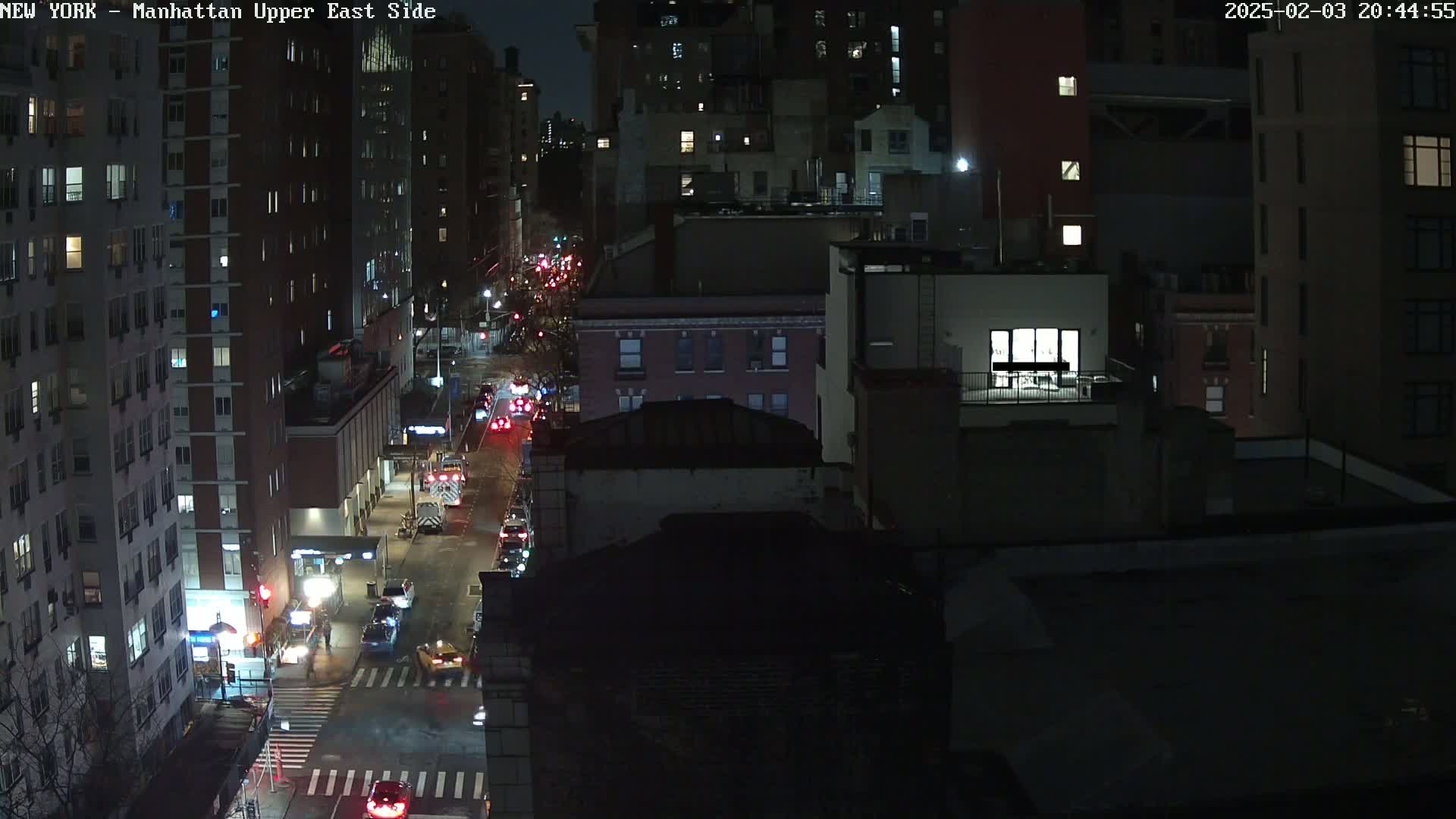 A nighttime, high-angle view of a city street with several vehicles and tall buildings, under clear skies.