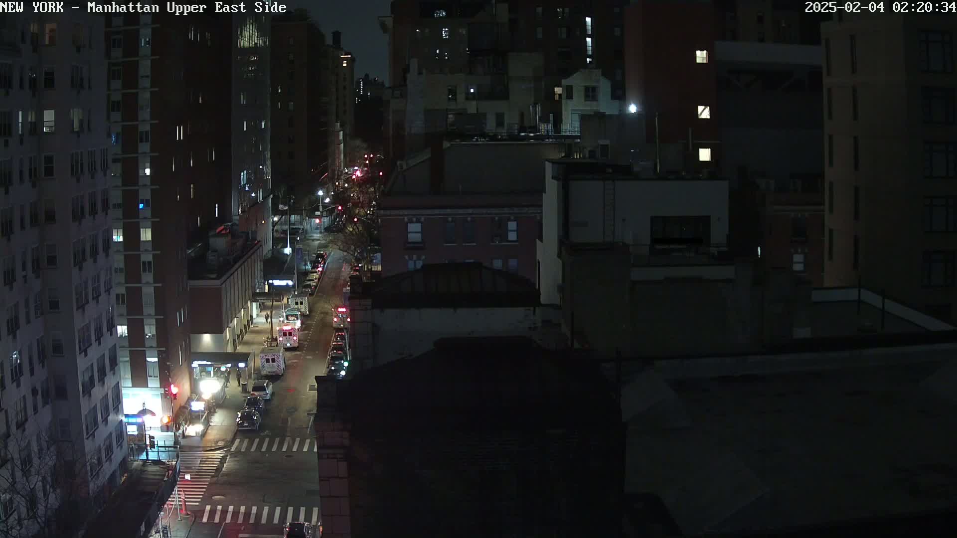 A nighttime, high-angle view of a city street with cars and buildings, under dark conditions.