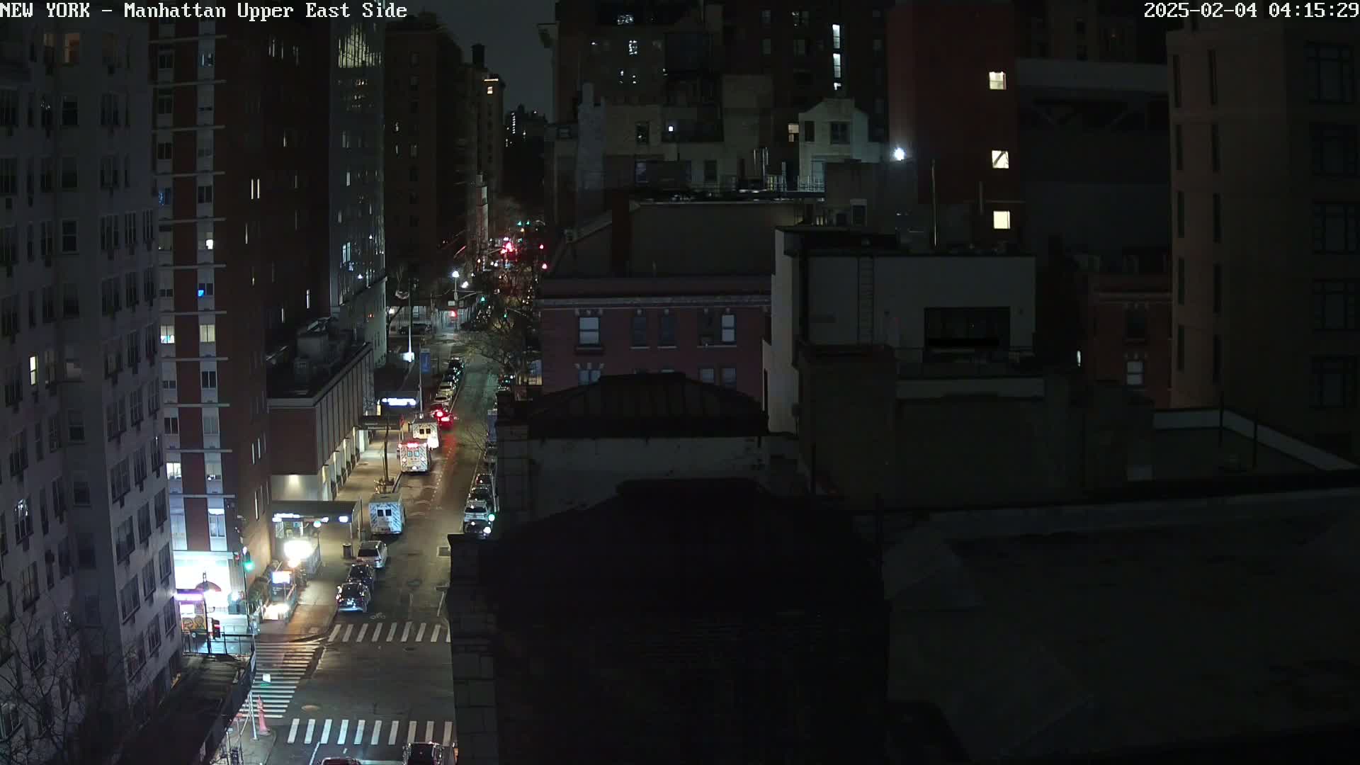 A nighttime, high-angle view of a city street with several vehicles, buildings, and streetlights.