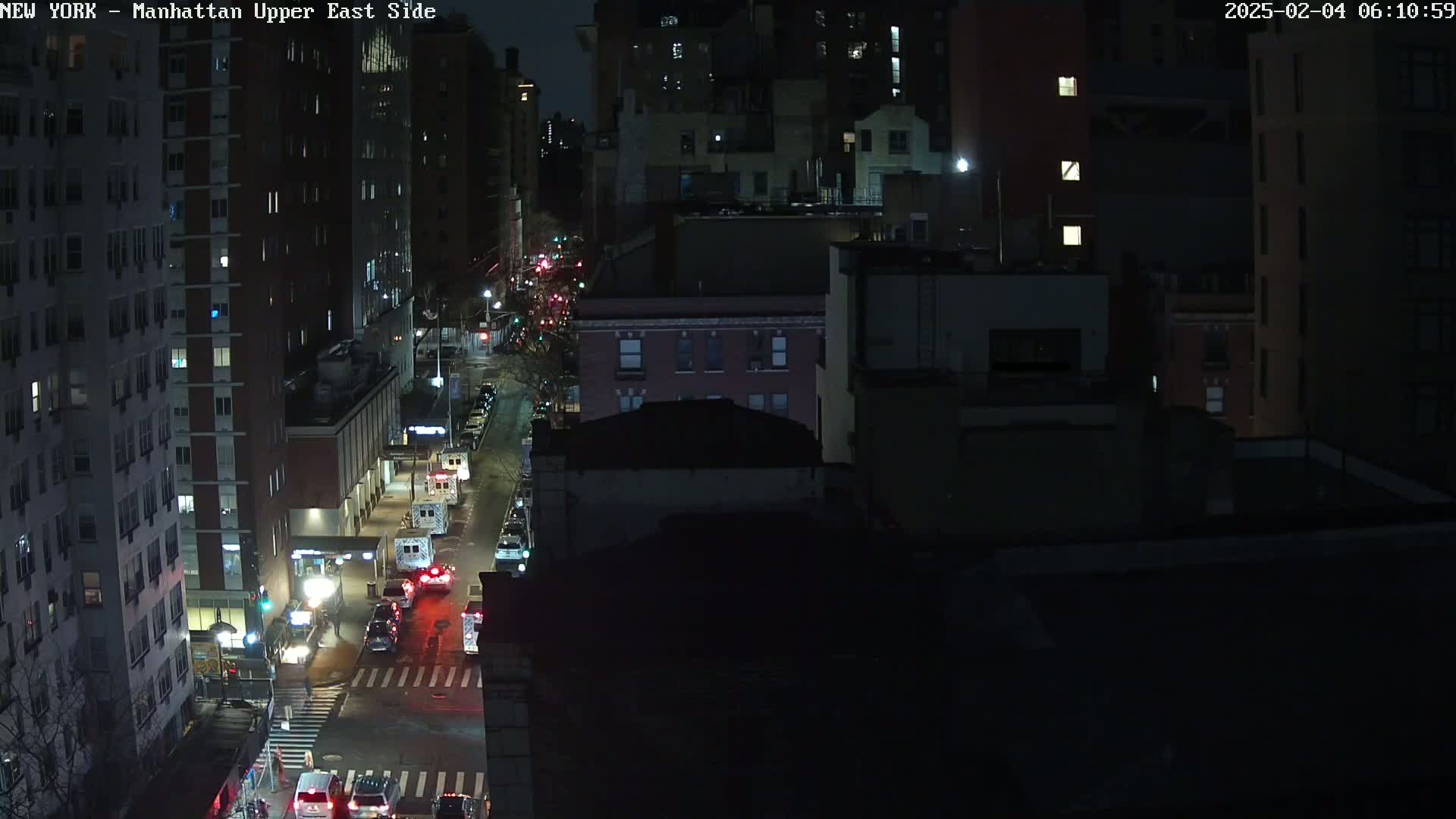 A nighttime aerial view shows a city street with several vehicles and buildings under dark, clear skies.
