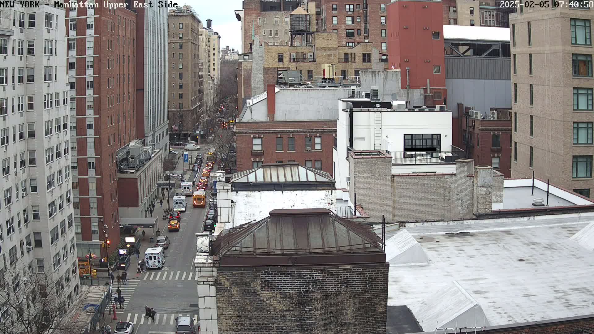 A high-angle view of a city street with traffic, mostly brick buildings, and a mostly cloudy sky.