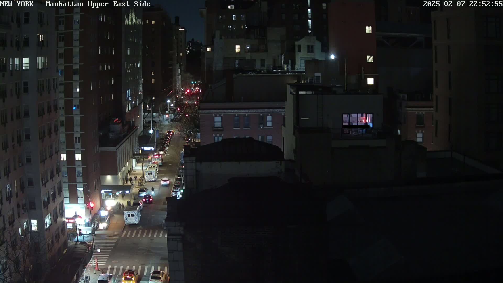 A nighttime, high-angle view of a city street with several vehicles and buildings, under clear skies.