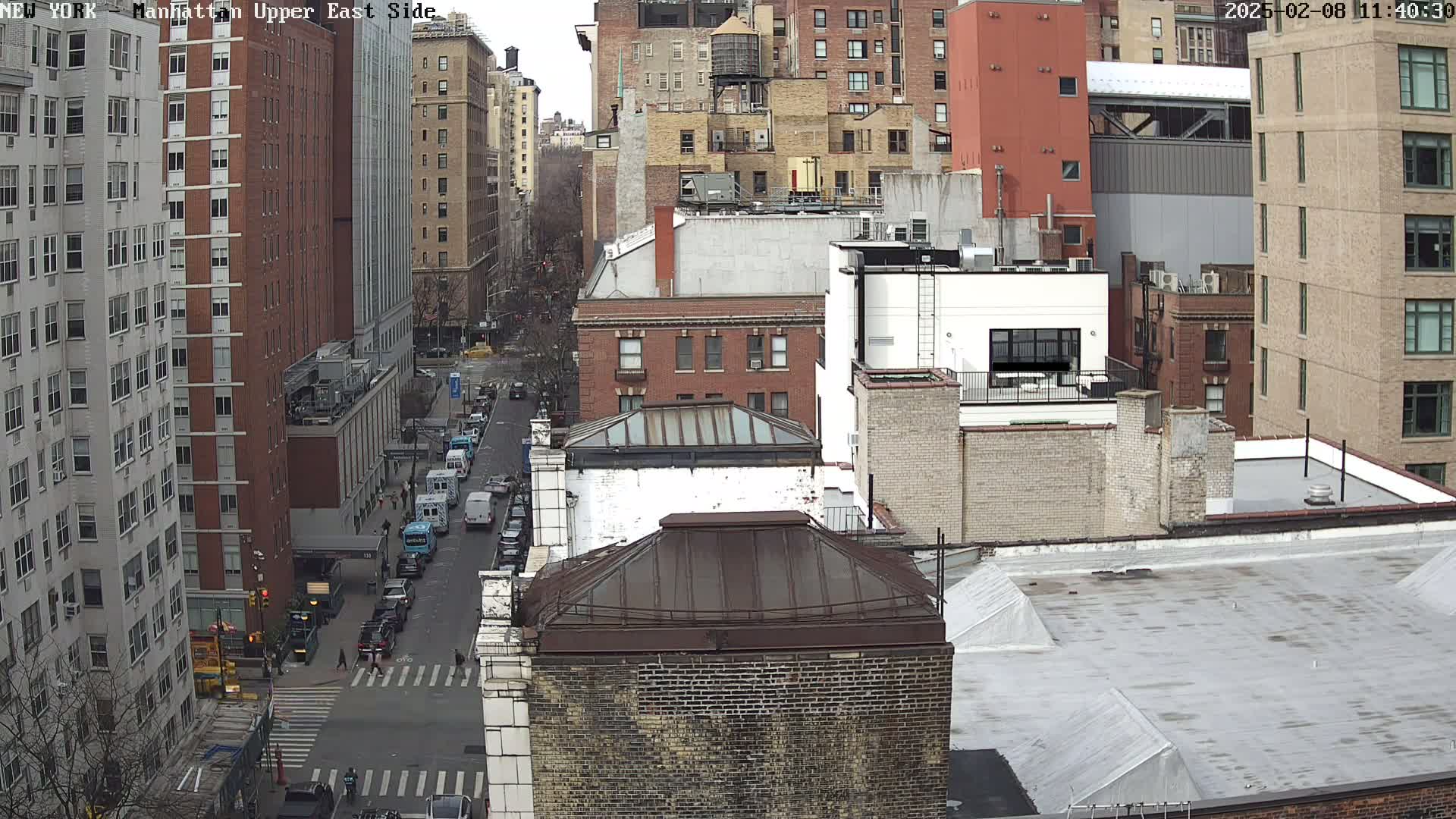 A high-angle view of city buildings on a cloudy day, showing a street with several parked cars and a crosswalk.