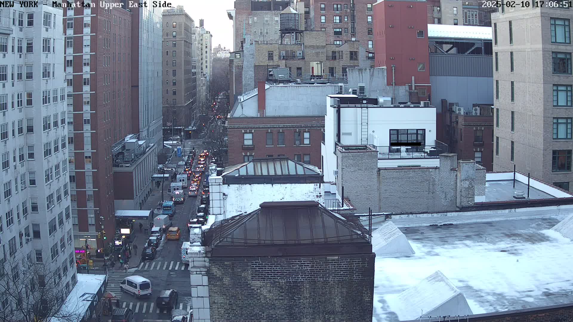 A high-angle view of a city street scene with buildings covered in snow, showing traffic on a street below.
