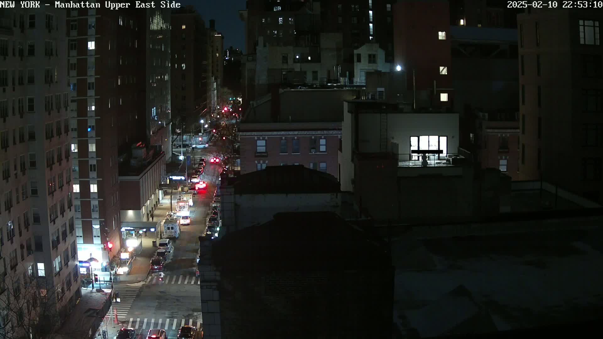 A nighttime, high-angle view of a city street with several cars and buildings, under a clear, dark sky.