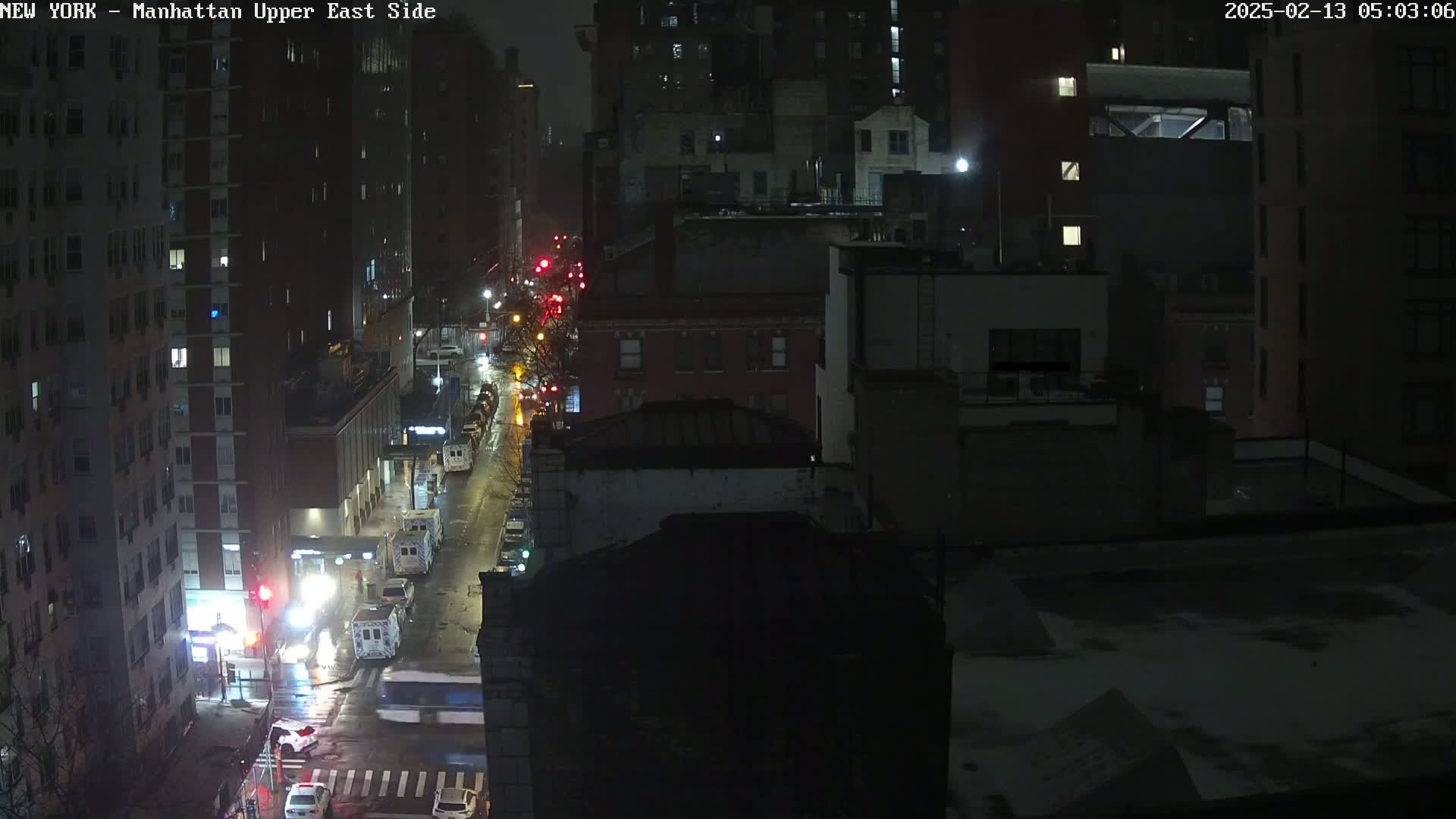 A nighttime aerial view of a city street with sparse traffic under snowy conditions.