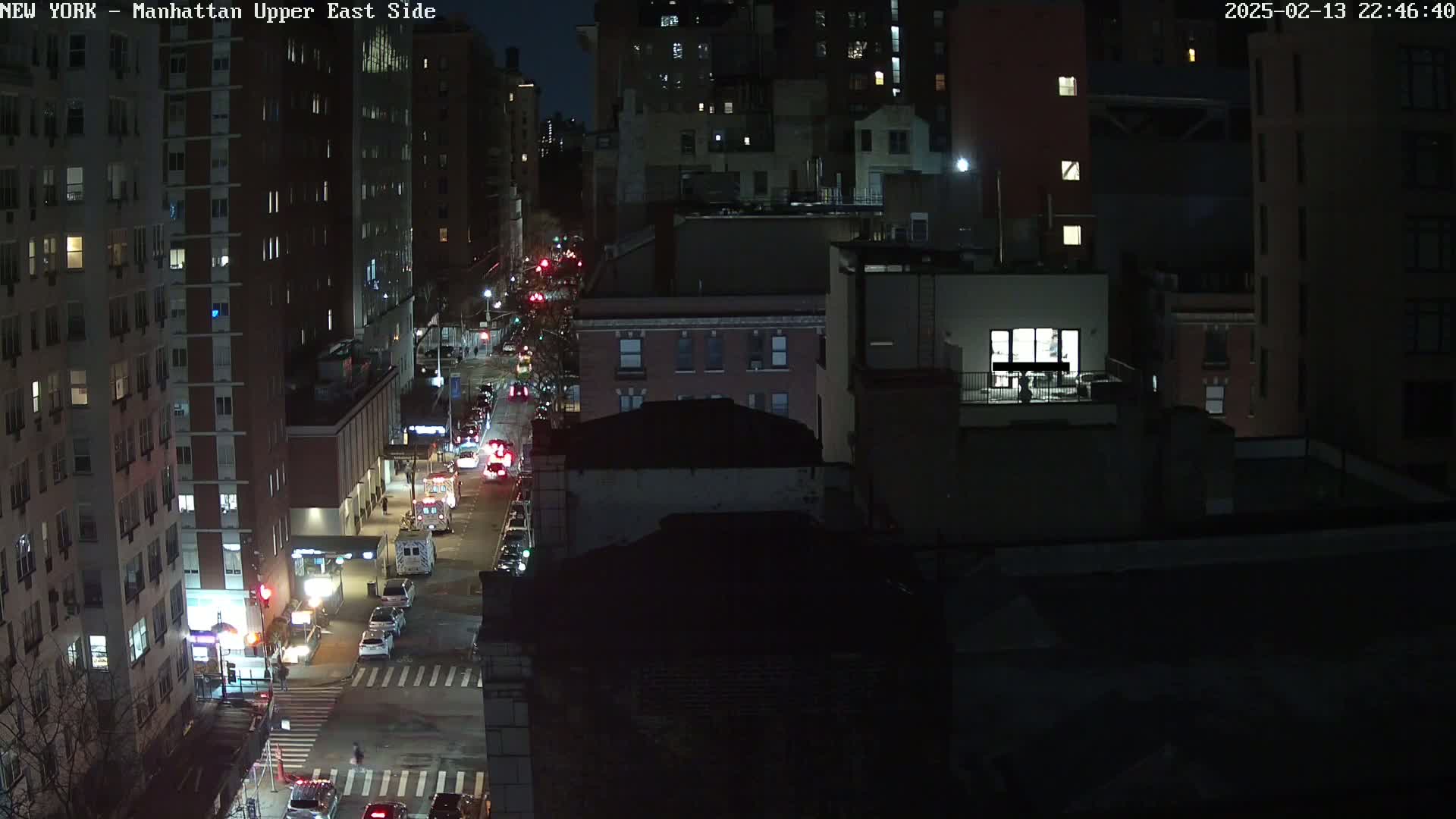 A nighttime aerial view of a city street with cars and buildings, under dark and clear skies.