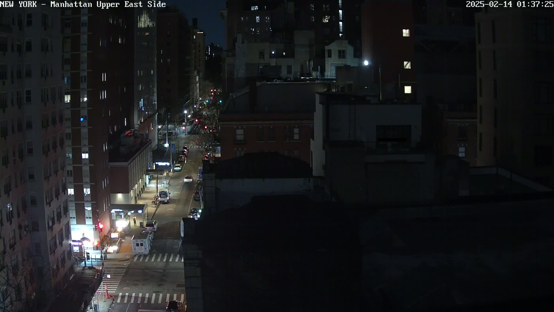 A nighttime, high-angle view of a city street with several vehicles and buildings under dark, clear skies.