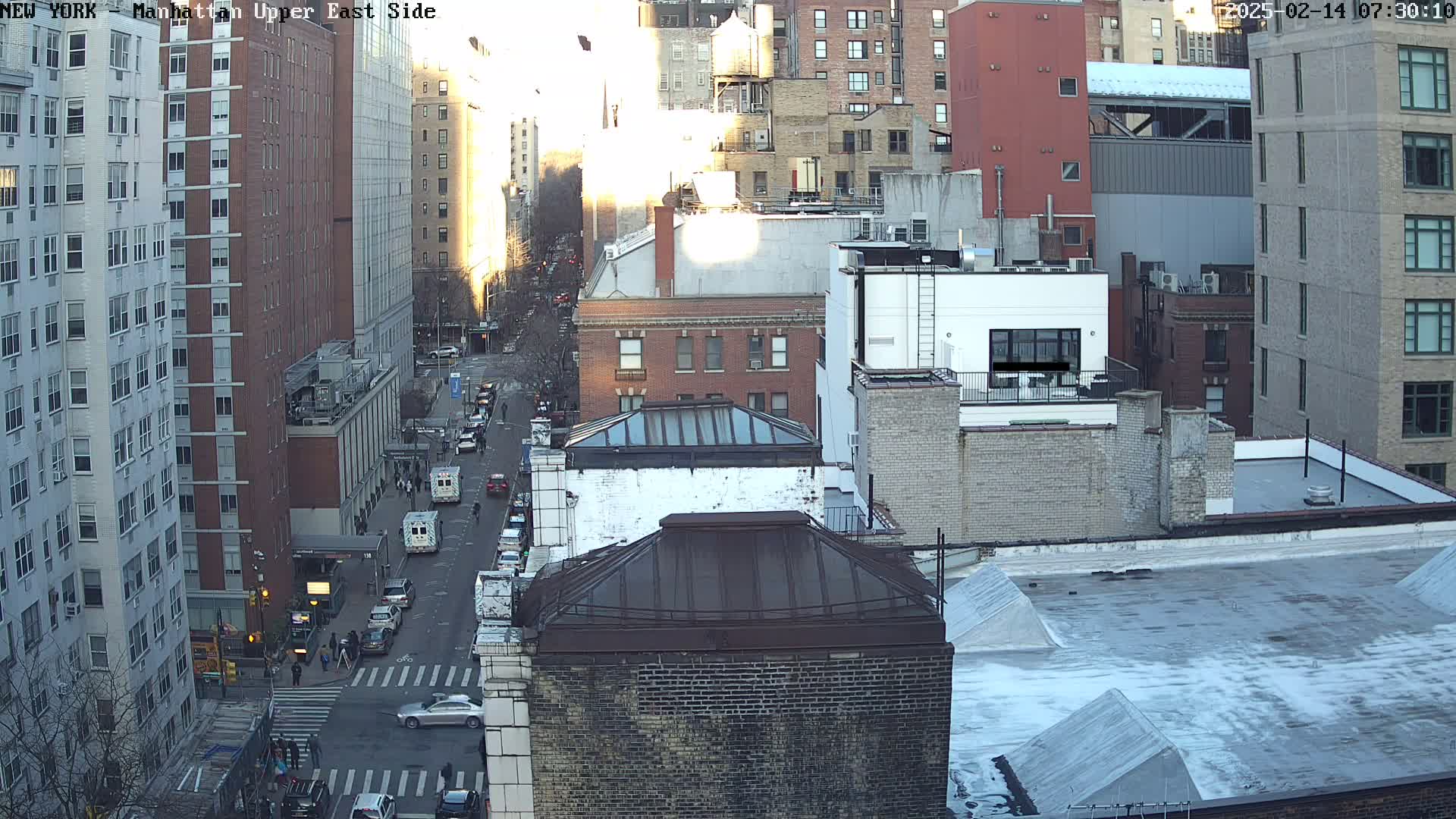 An aerial view of a city street with several multi-story buildings, under a partly sunny sky.
