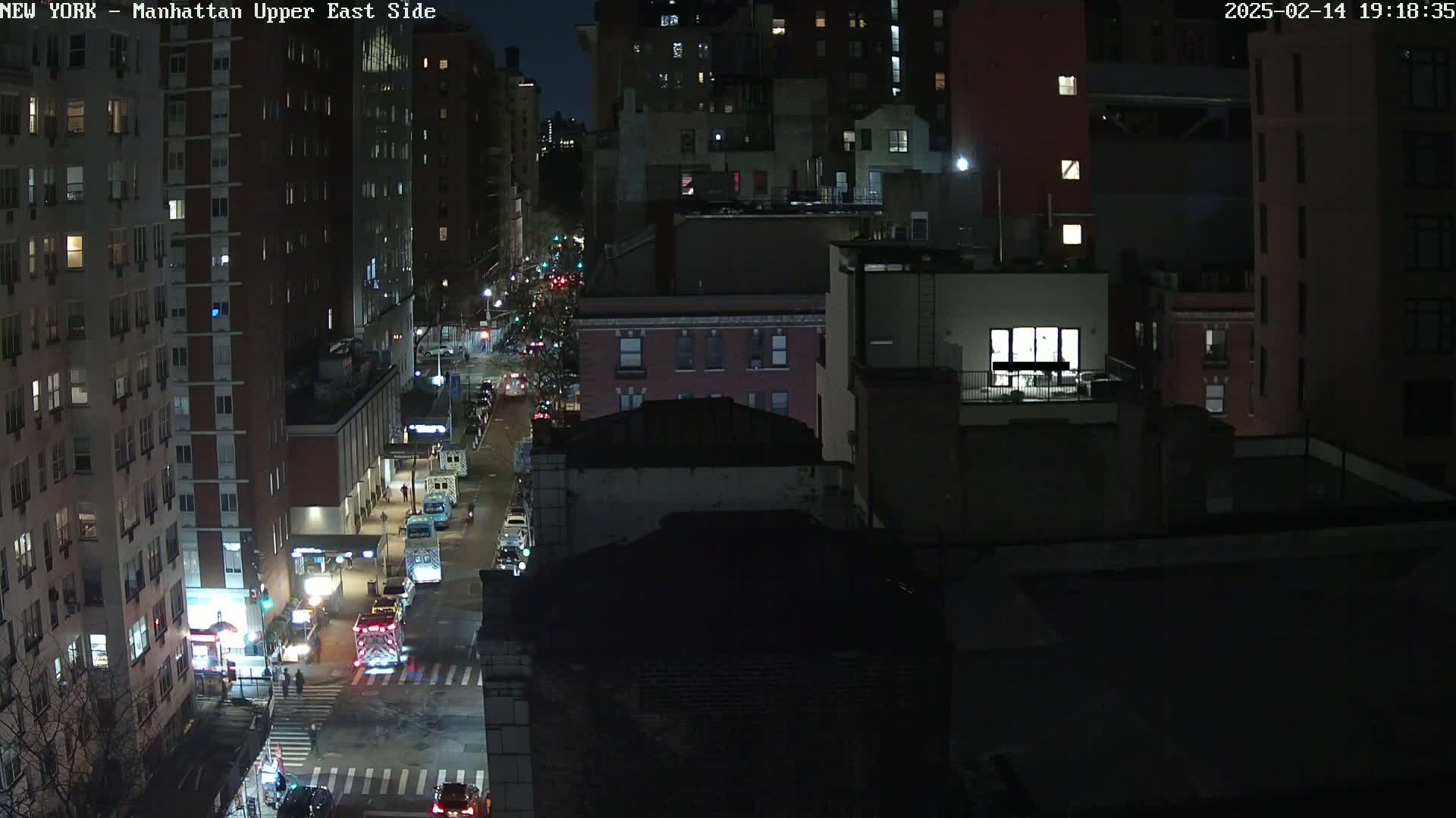 A nighttime aerial view of a city street with traffic and buildings, under dark, clear conditions.