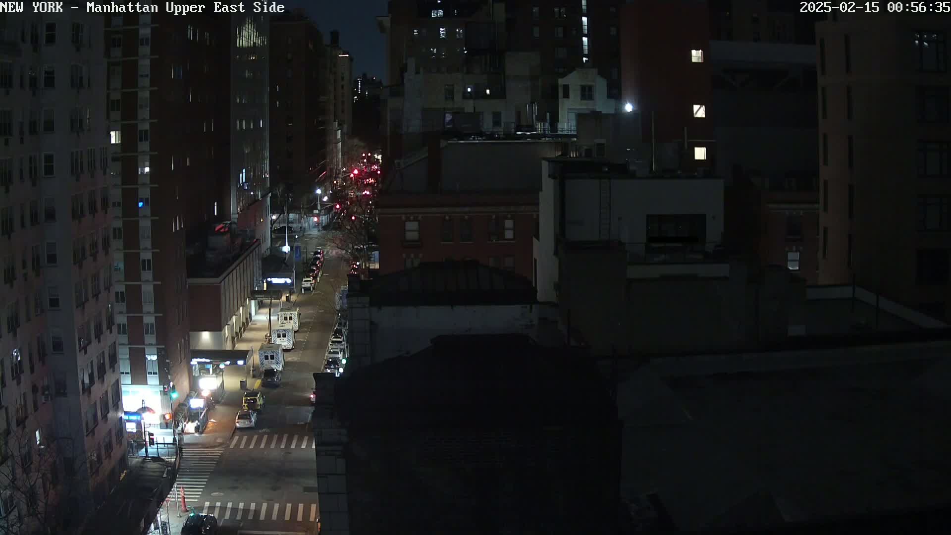 A nighttime, high-angle view of a city street with several vehicles and tall buildings illuminated by streetlights.
