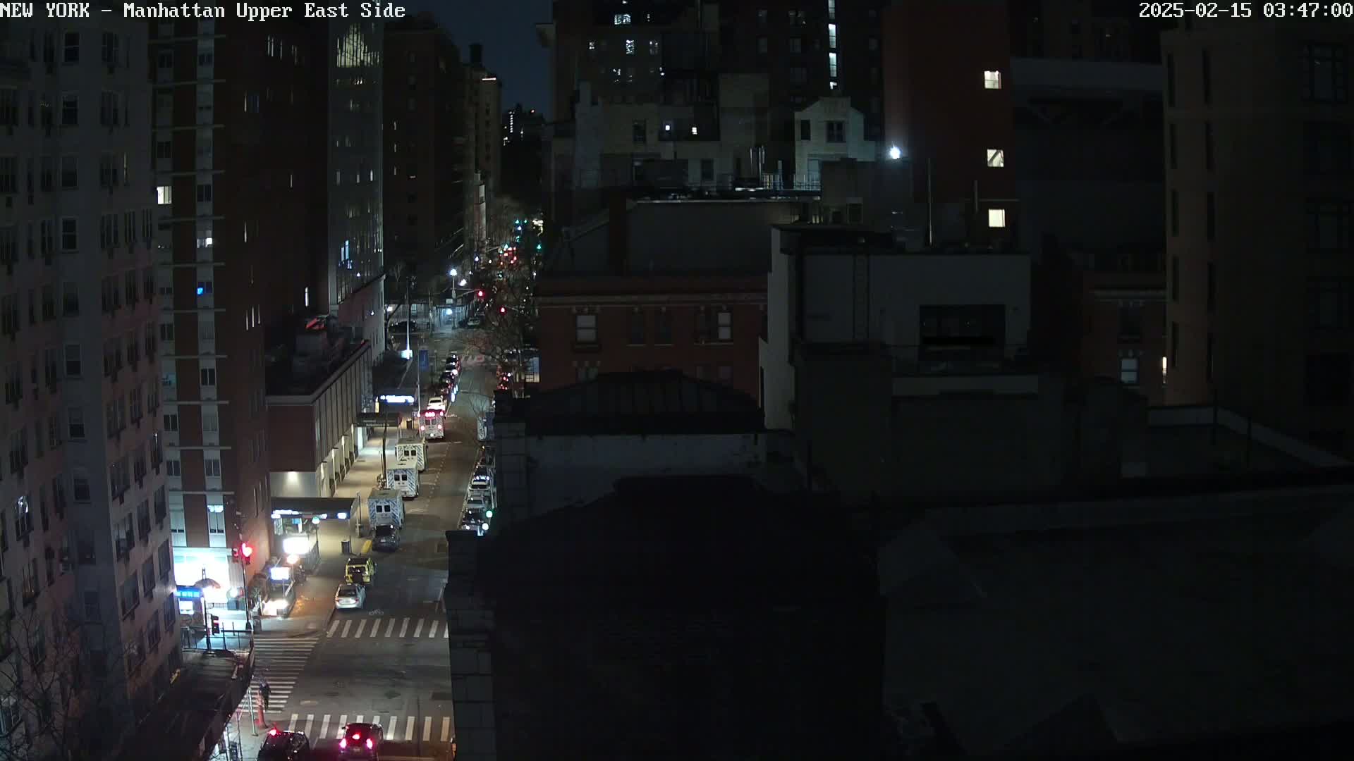 A nighttime, high-angle view of a city street with several vehicles and tall buildings on either side.