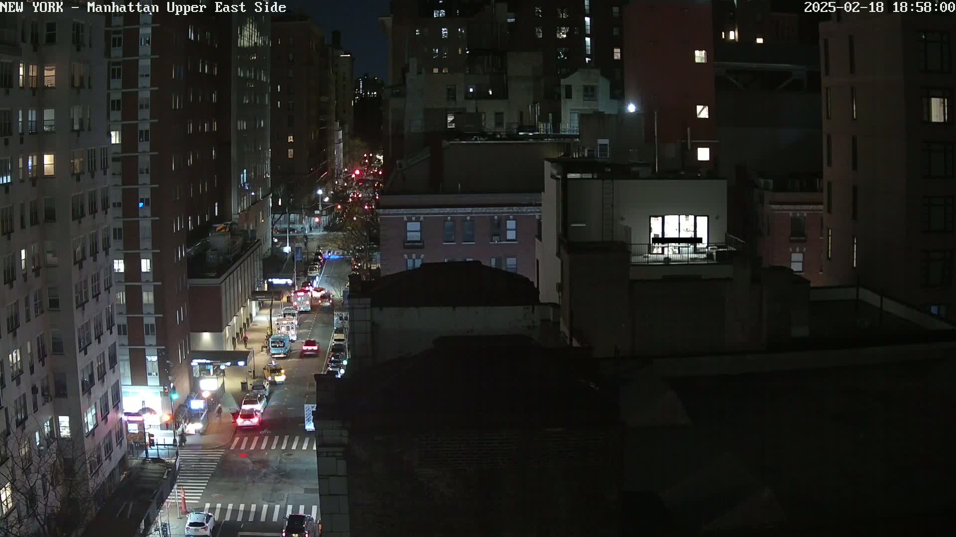 A nighttime aerial view of a city street with cars driving, showing several multi-story buildings.