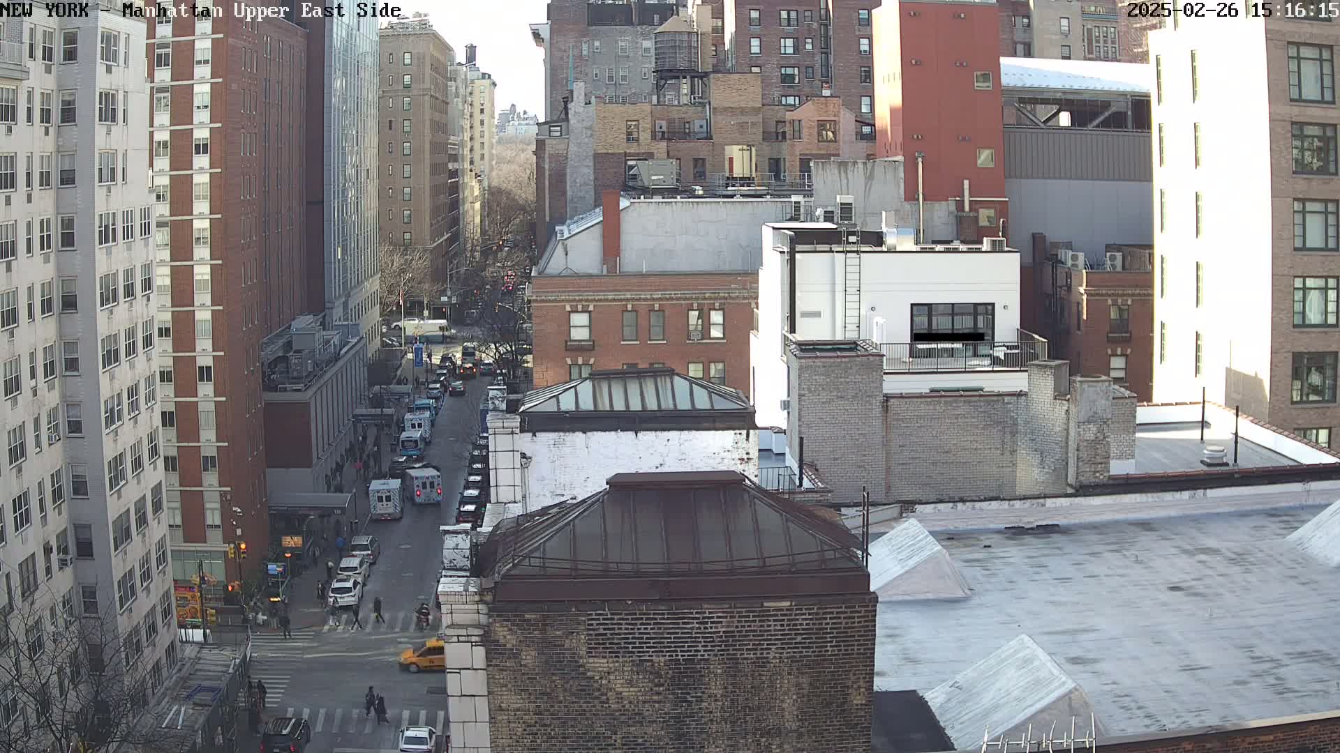 A sunny, high-angle view of a city street, showing several multi-story buildings and vehicles on the road below.