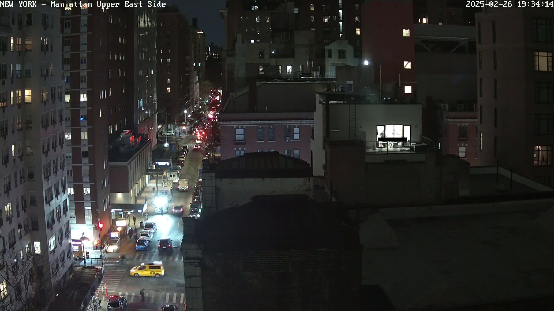 A nighttime aerial view of a city street with traffic and several multi-story buildings.