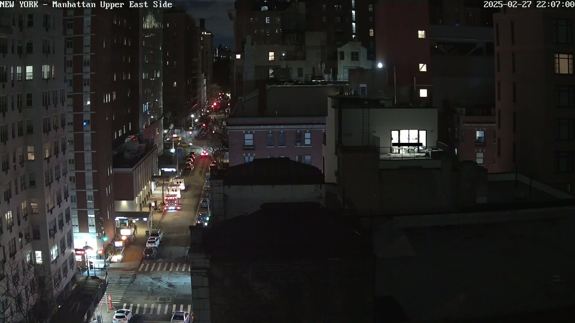 A nighttime, high-angle view of a city street with several cars and buildings, showing some traffic and lights on.