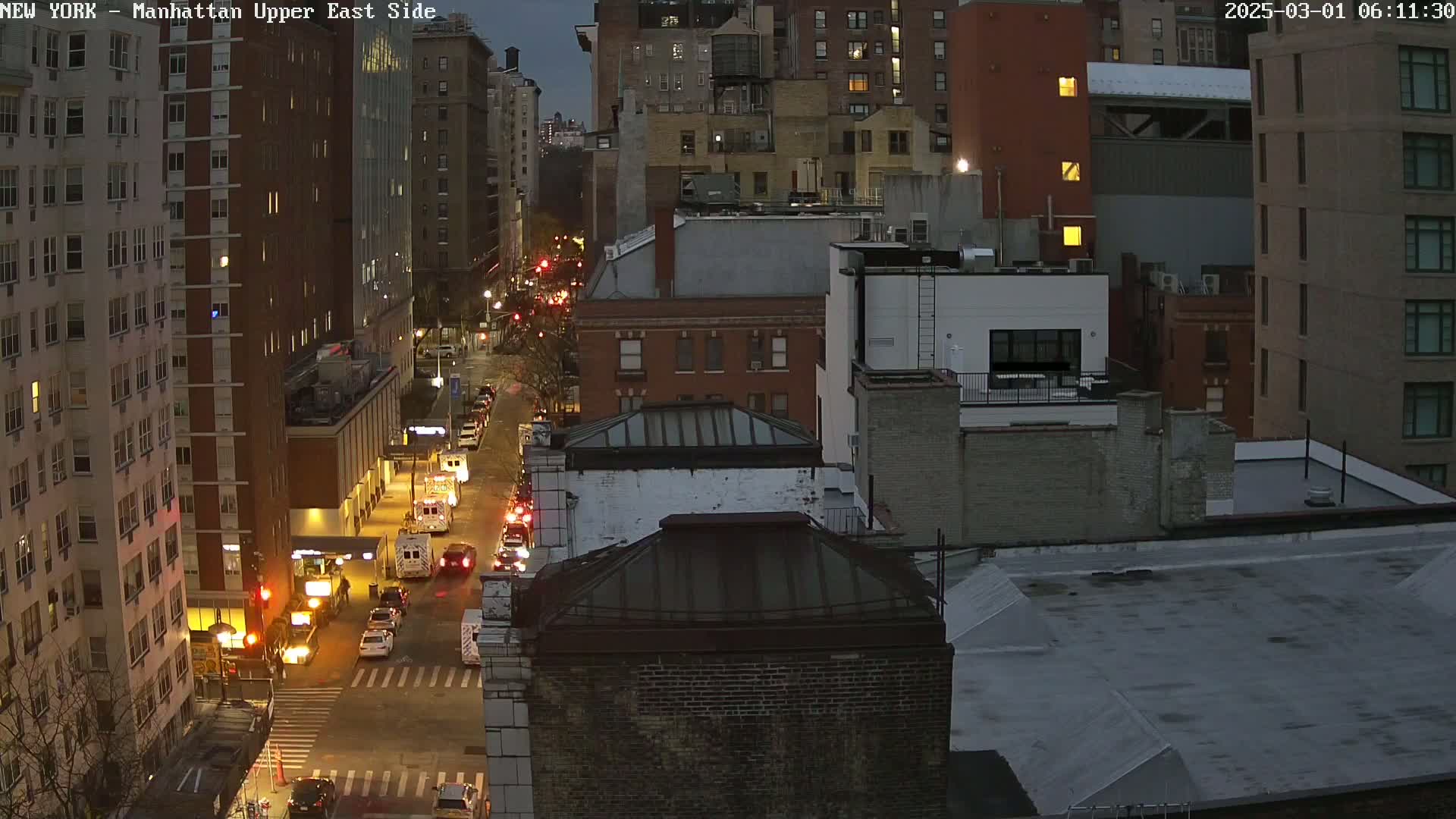 A twilight view of a city street at night, showing traffic and several multi-story buildings.