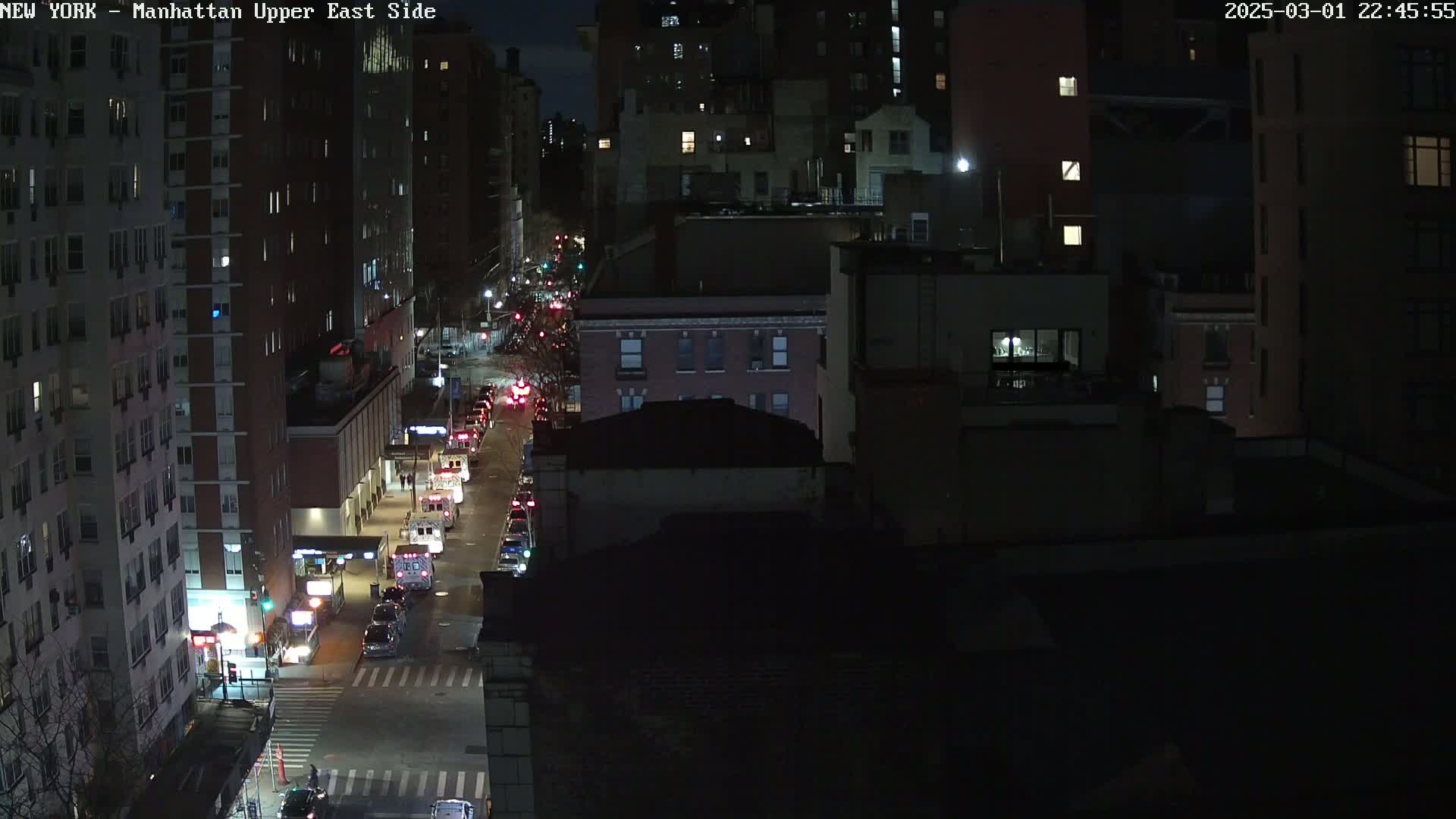 A nighttime, high-angle view of a city street with several vehicles and tall buildings under a dark sky.