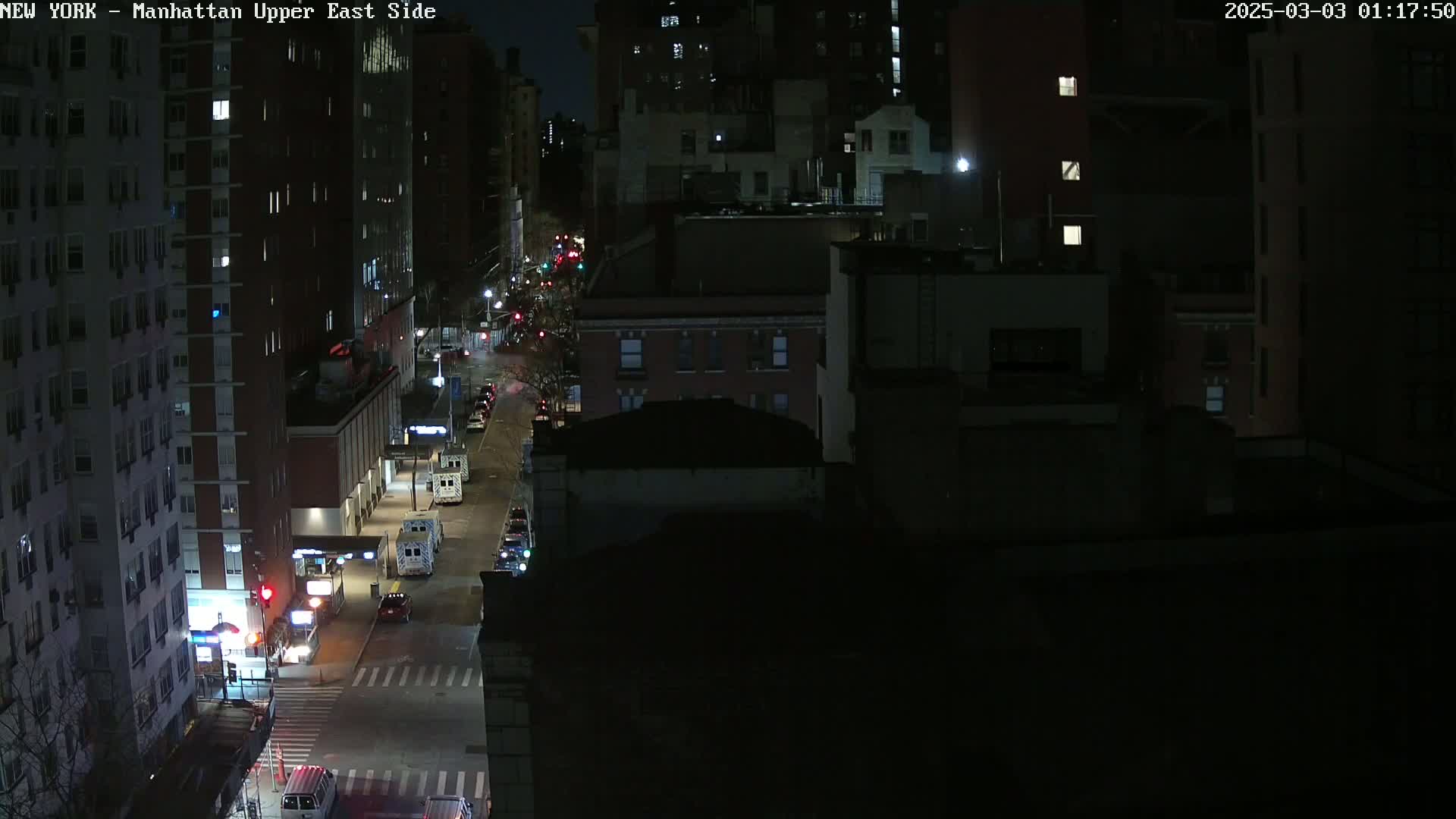 A nighttime aerial view shows city streets with several vehicles and buildings, under clear skies.