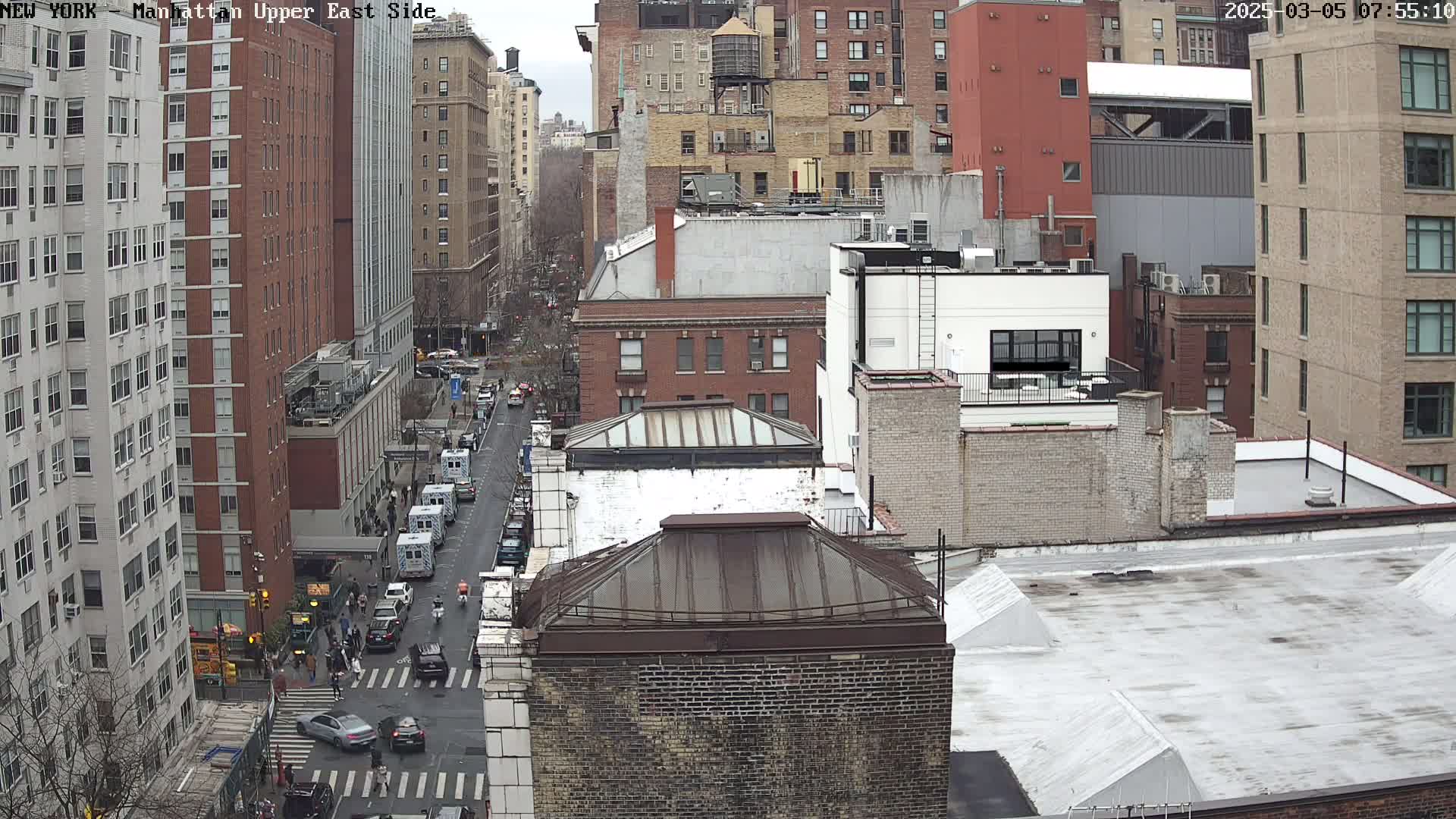 A high-angle view of a city street scene on an overcast day, showing several multi-story brick buildings and vehicles on a street below.