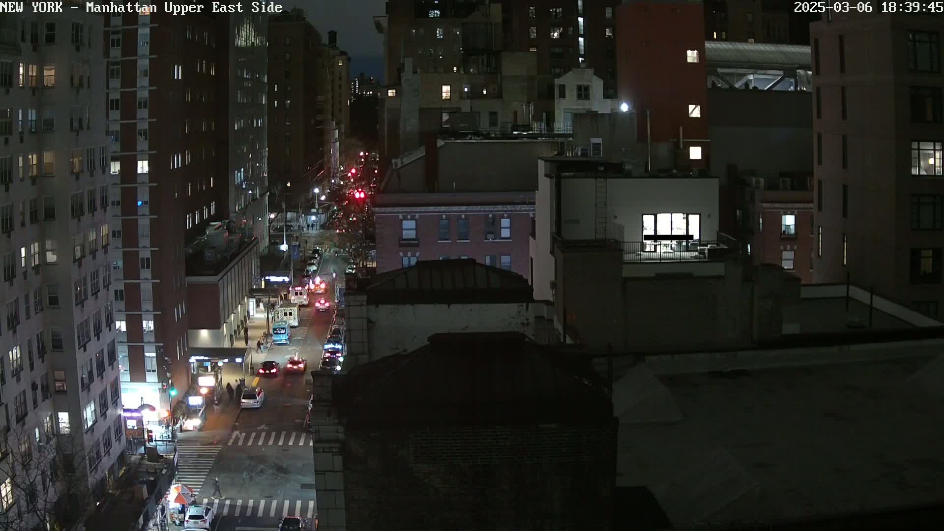 A nighttime aerial view of a city street with several buildings and cars driving on a road.