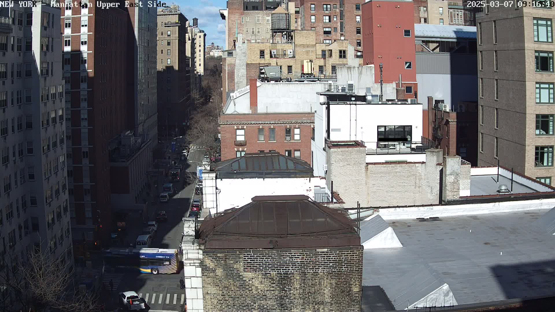 A sunny day view of a city street, showing several multi-story brick buildings and vehicles traveling on the street below.
