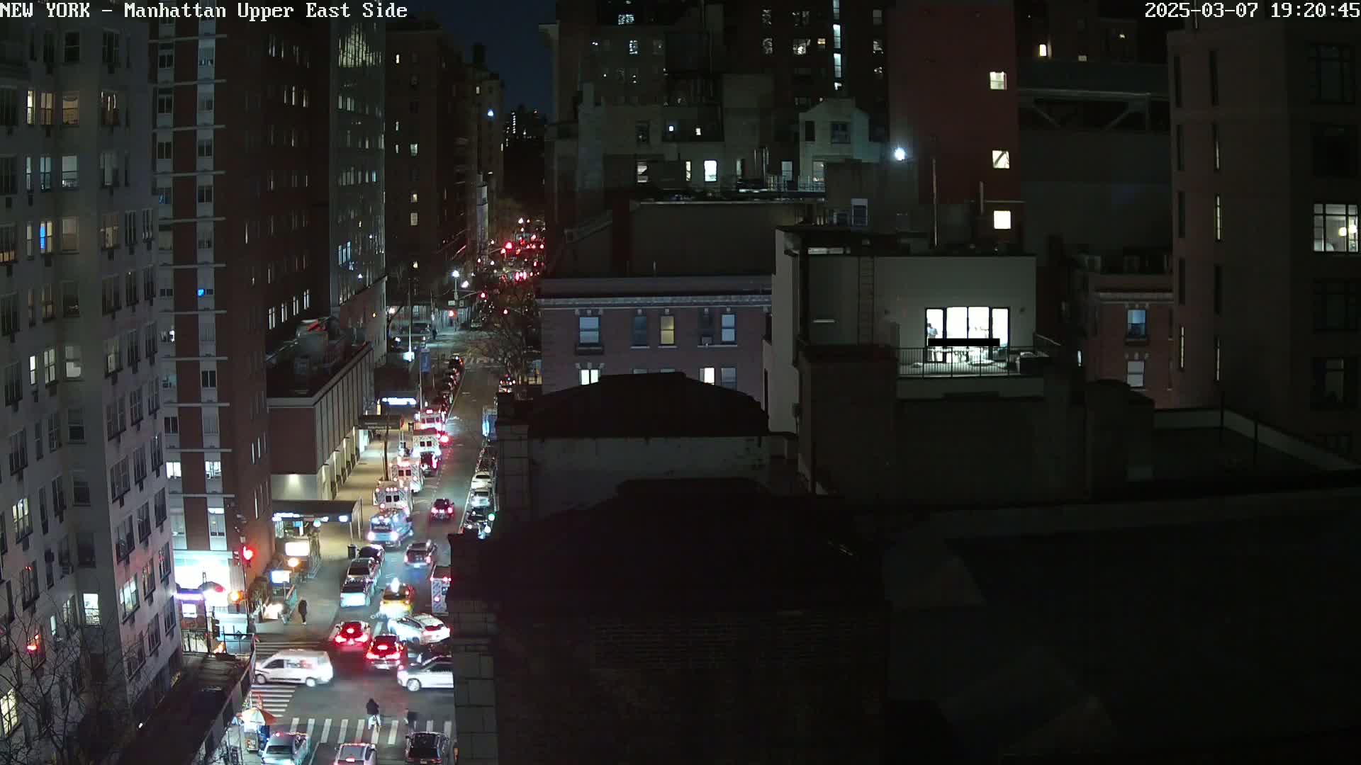 A nighttime aerial view of a city street with traffic, illuminated by streetlights and building lights, under a dark sky.