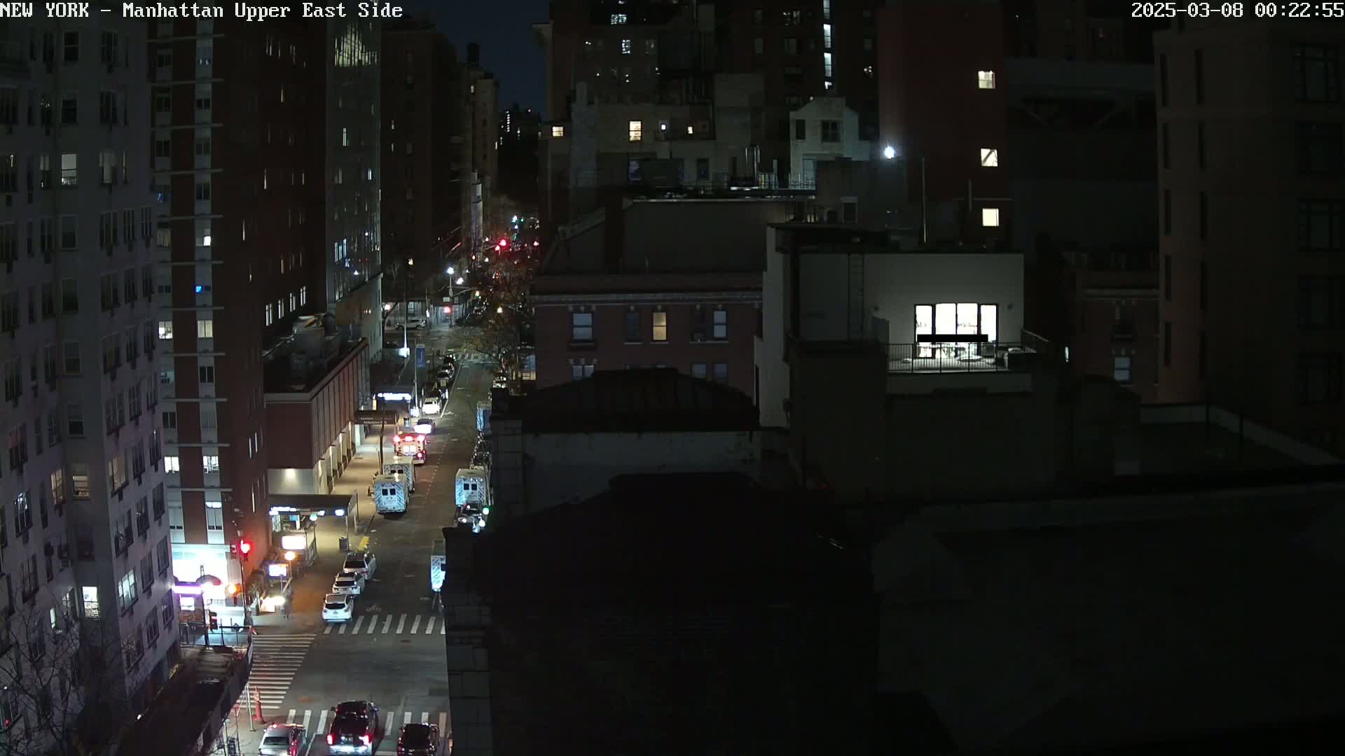 A nighttime, high-angle view of a city street with several vehicles and buildings, illuminated by streetlights and building lights.