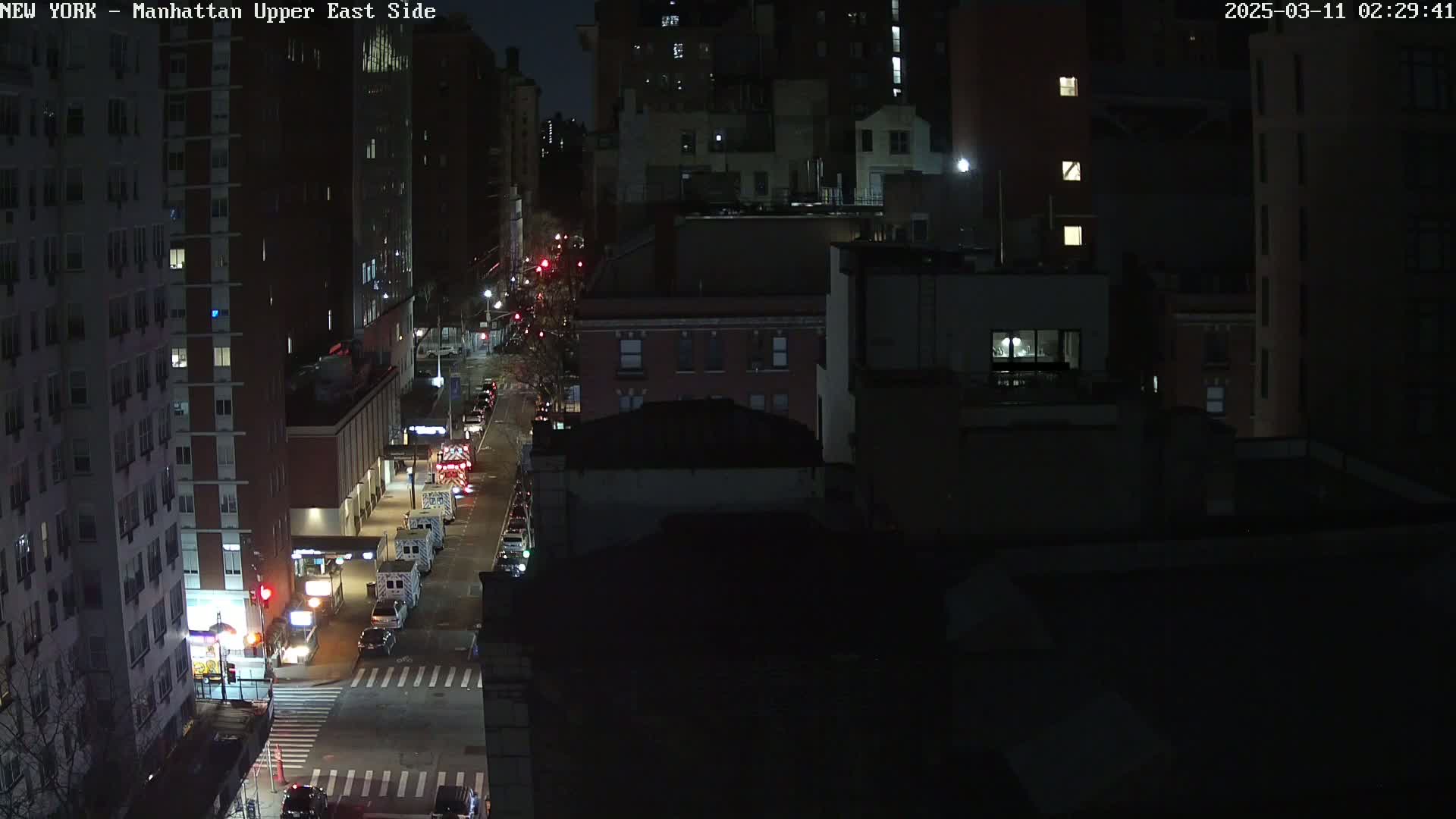A nighttime, high-angle view of a city street with several emergency vehicles parked alongside buildings.